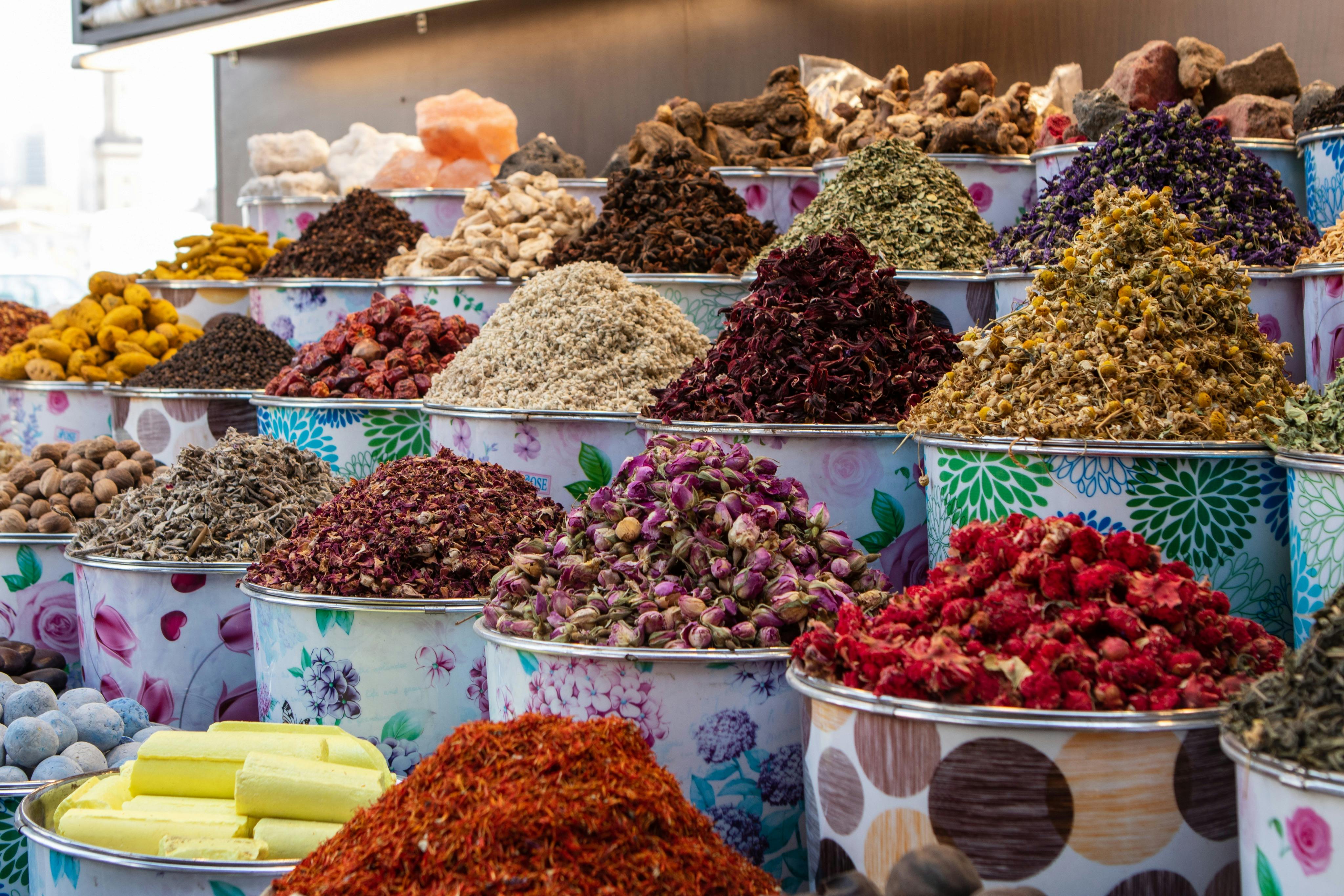 Various colorful spices and dried herbs displayed in ornate bowls at a market.