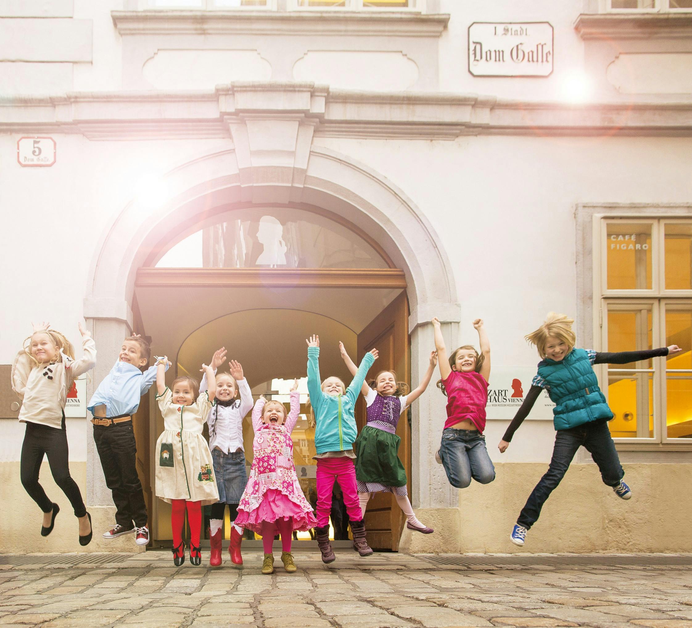 Před klenutými dveřmi na dlážděném nádvoří radostně skočí devět dětí s cedulí s nápisem „Dom Galle“.