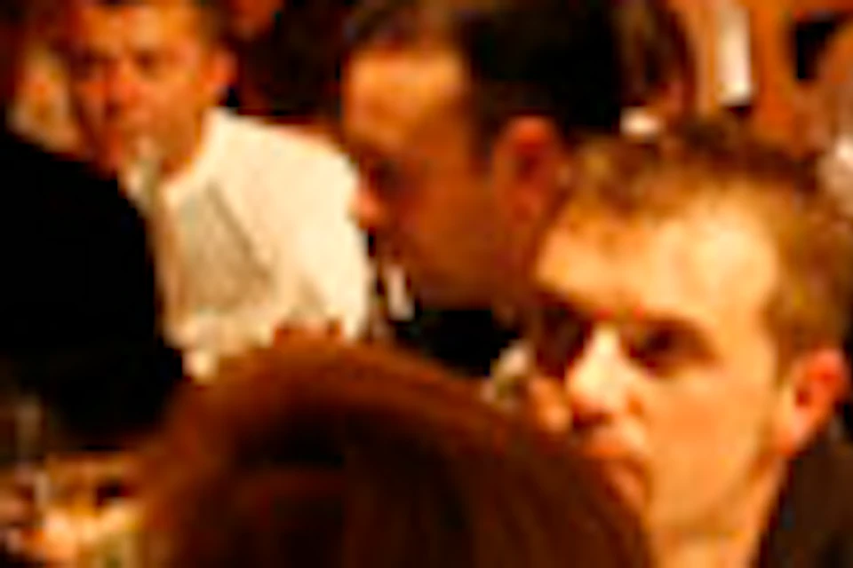 Dimly lit restaurant with wooden beams on the ceiling, crowded with seated diners and a waiter in motion.