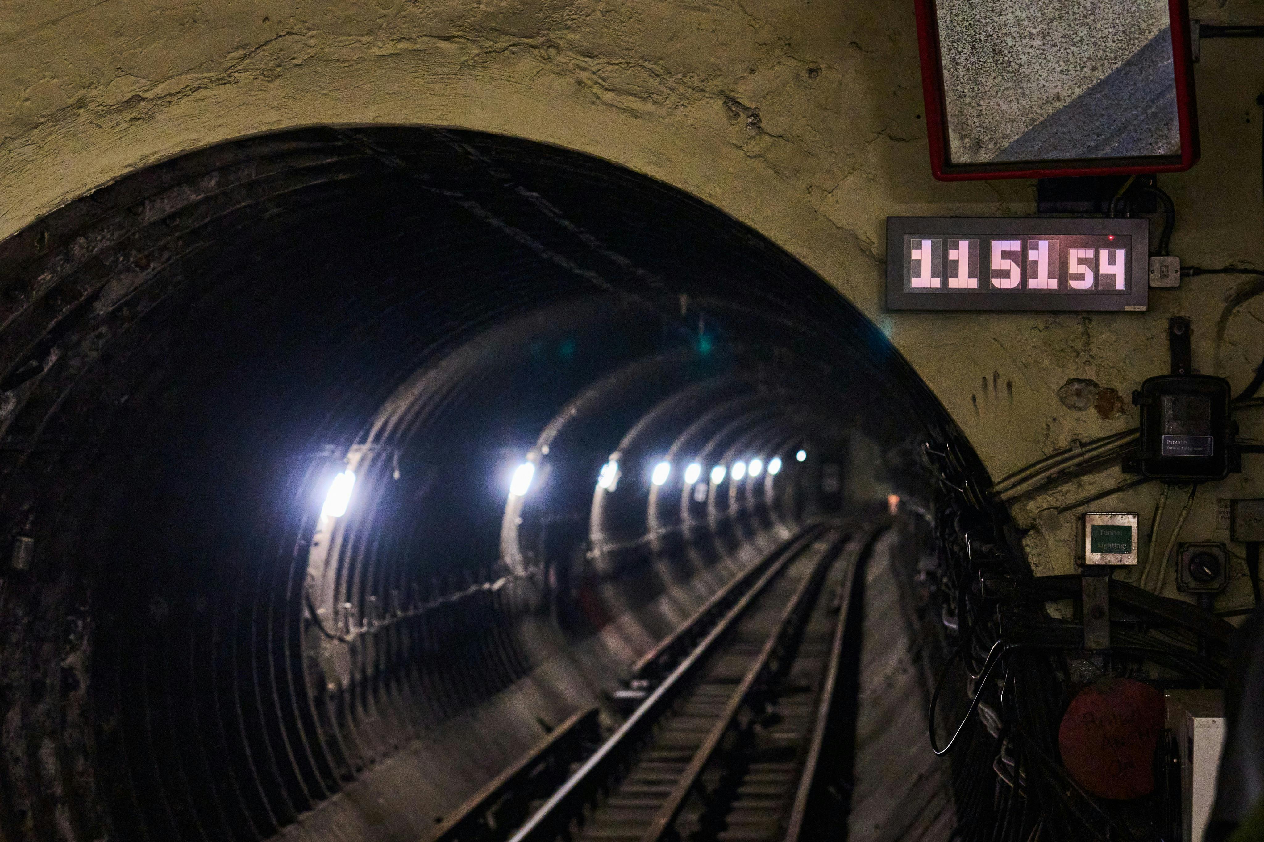 Een metrotunnel met verlichte lampen langs de wanden en treinrails die zich in de verte uitstrekken.
