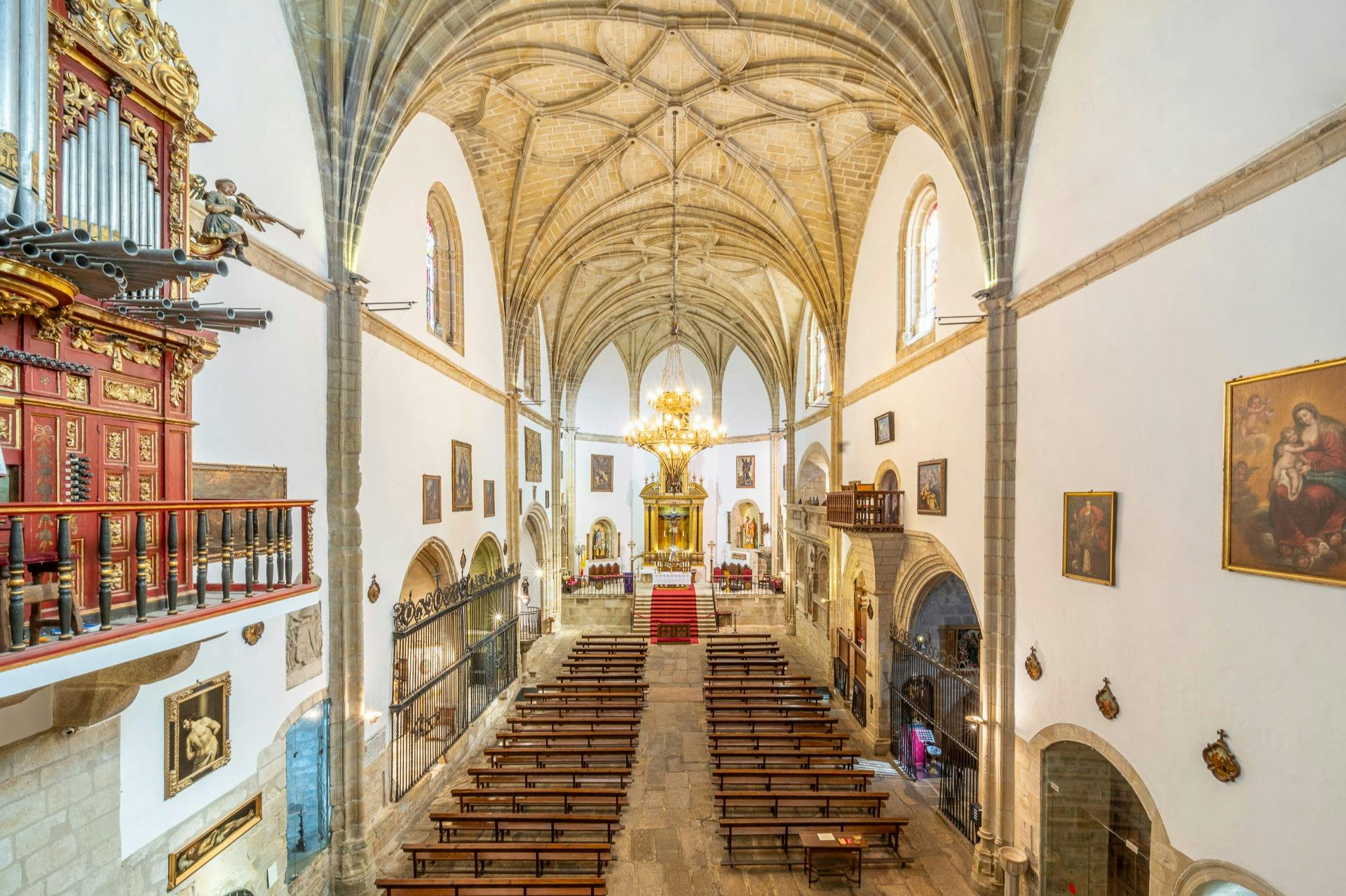 Interiér kostela s klenutým stropem, dřevěnými lavicemi, lustry, píšťalovými varhanami a náboženskými uměleckými díly na stěnách.