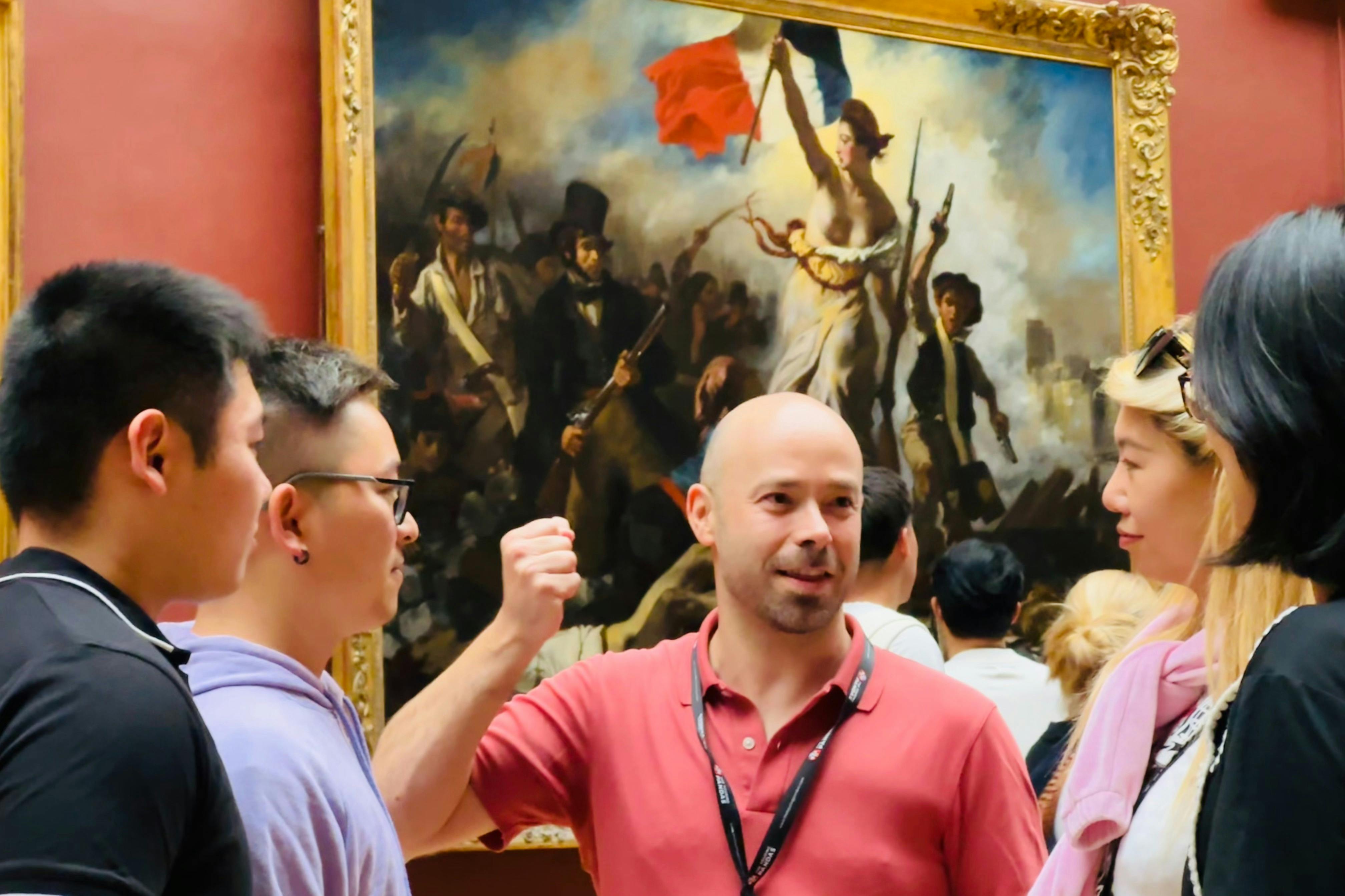 붉은 셔츠를 입은 남성이 깃발을 들고 있는 여성과의 전투 장면을 묘사한 유명한 그림 앞에서 두 사람을 안내합니다.