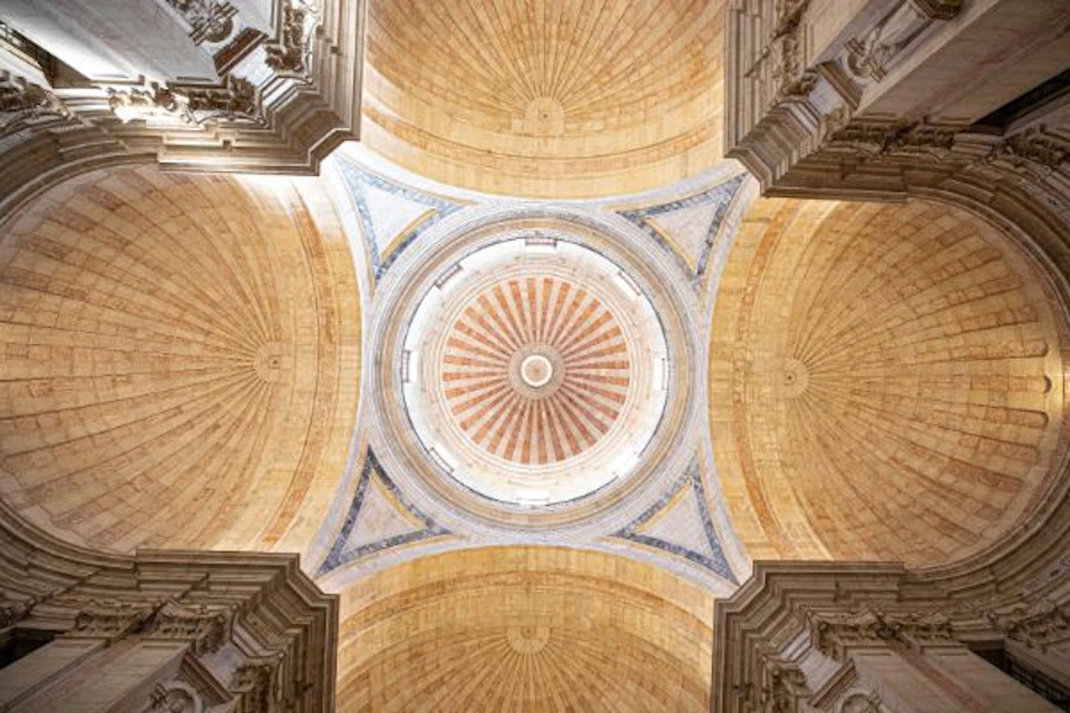 Ornate dome ceiling with intricate carvings and concentric patterns in warm hues, framed by multiple arches.