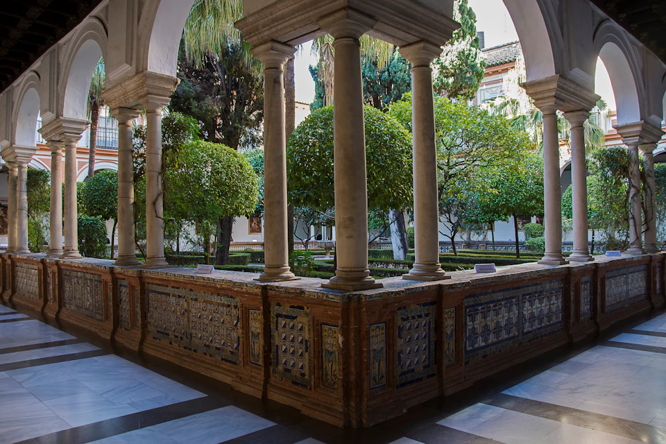 Ornate courtyard with tiled walls and stone columns, surrounded by lush green trees and shrubs.