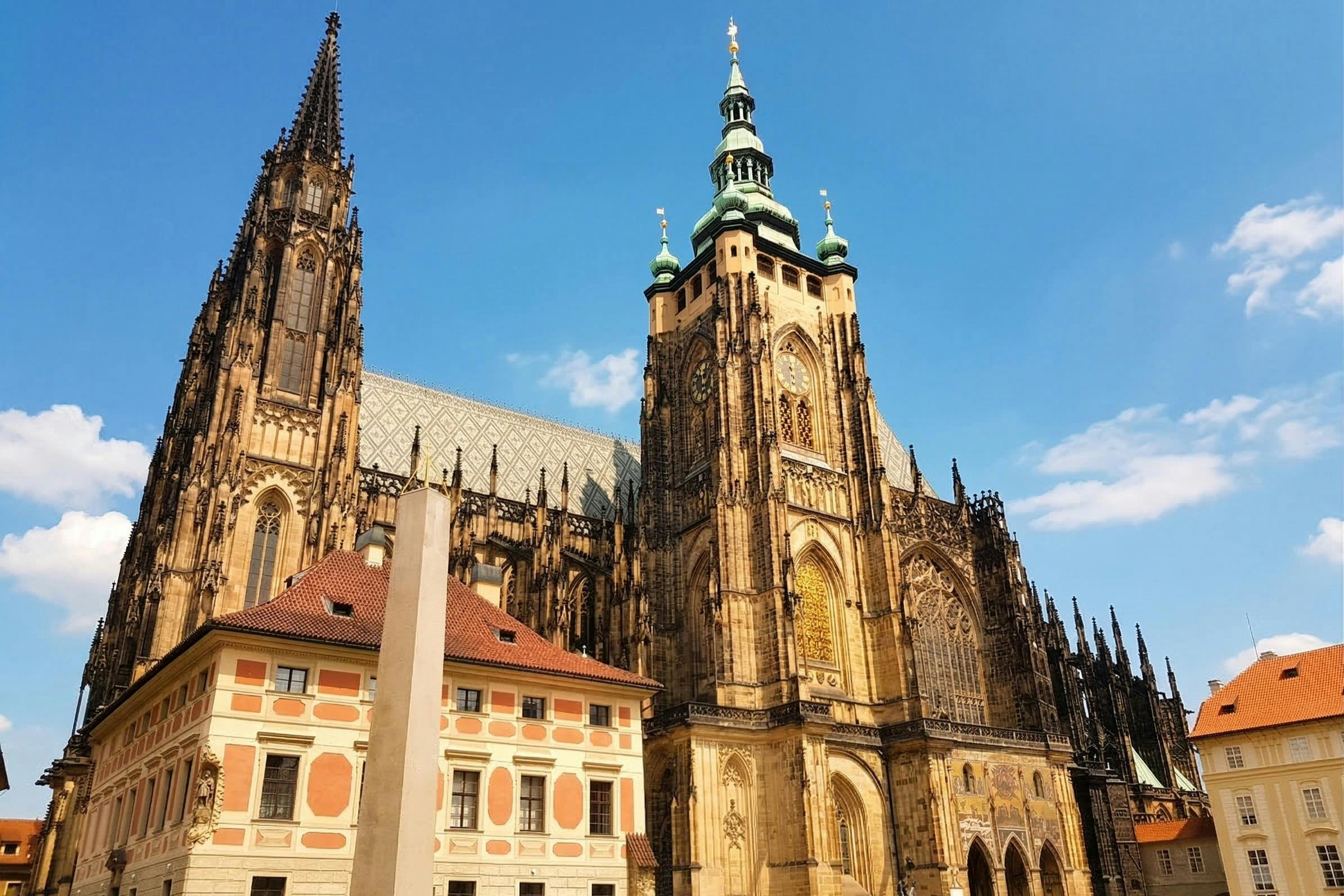 Gothic cathedral with intricate spires and a red-roofed building in front under a clear blue sky.