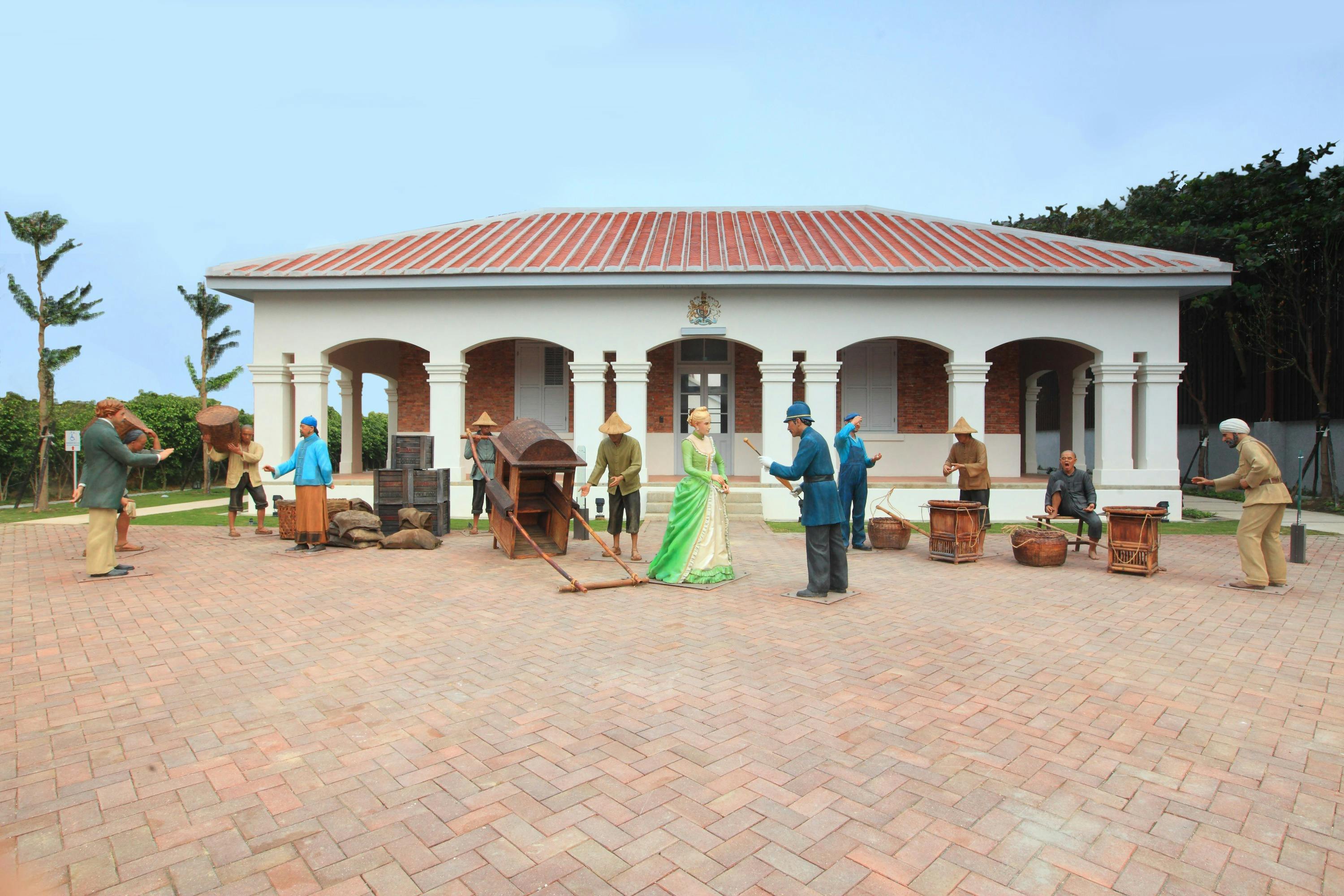 A historical scene with statues depicting people in traditional attire outside a colonial-style building.