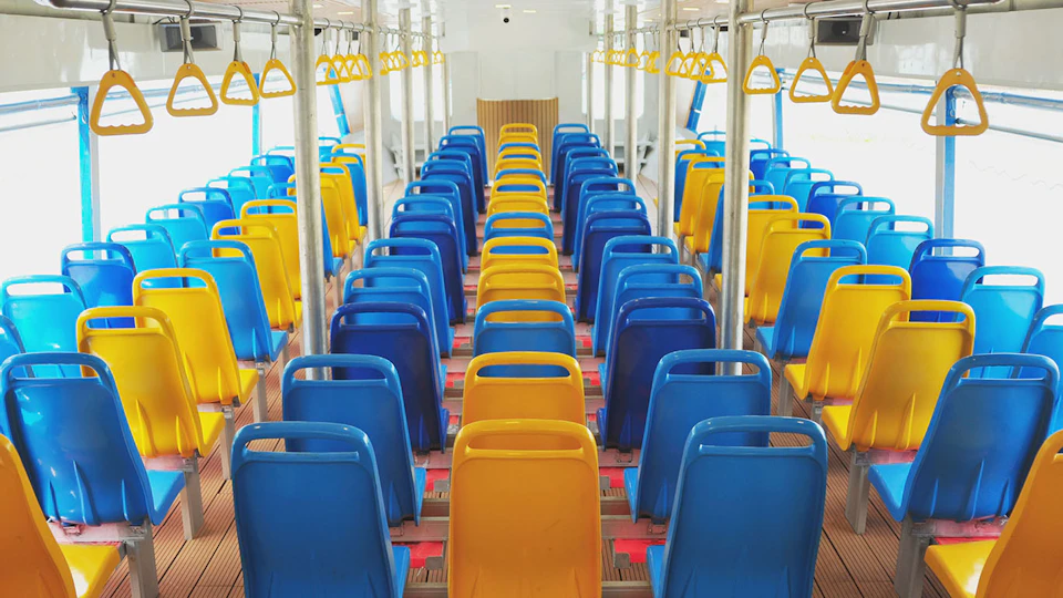 Interior of a bus with rows of blue and yellow plastic seats and overhead yellow handrails.