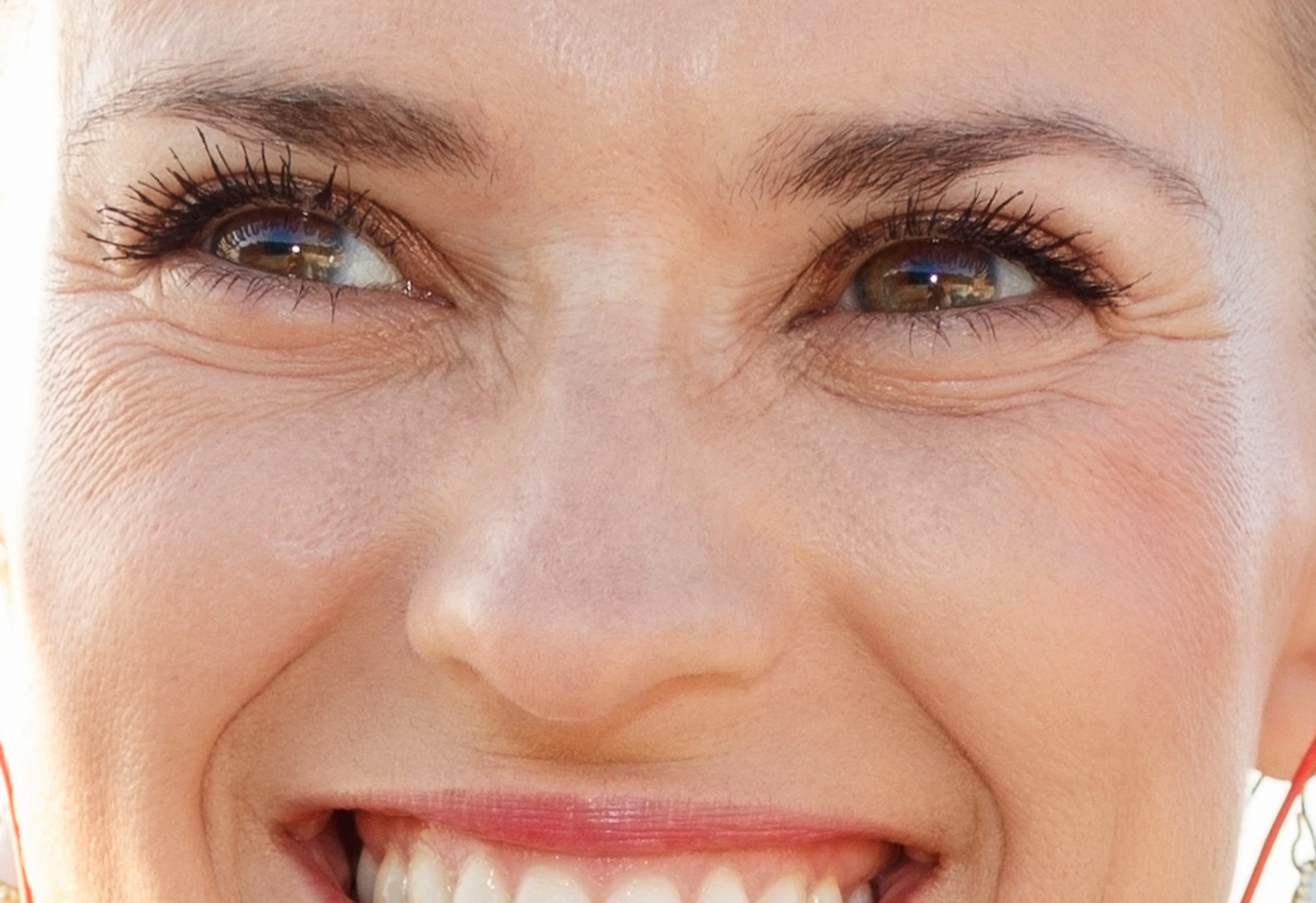 Woman smiling, holding a book, and wearing earphones. Mosaic tile bench and blurred cityscape in the background.
