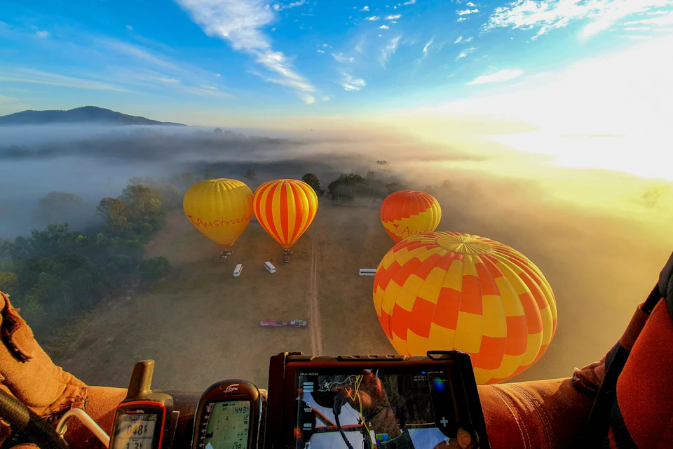 Hot air balloons float above misty fields at sunrise; a control panel and instruments are visible in the foreground.