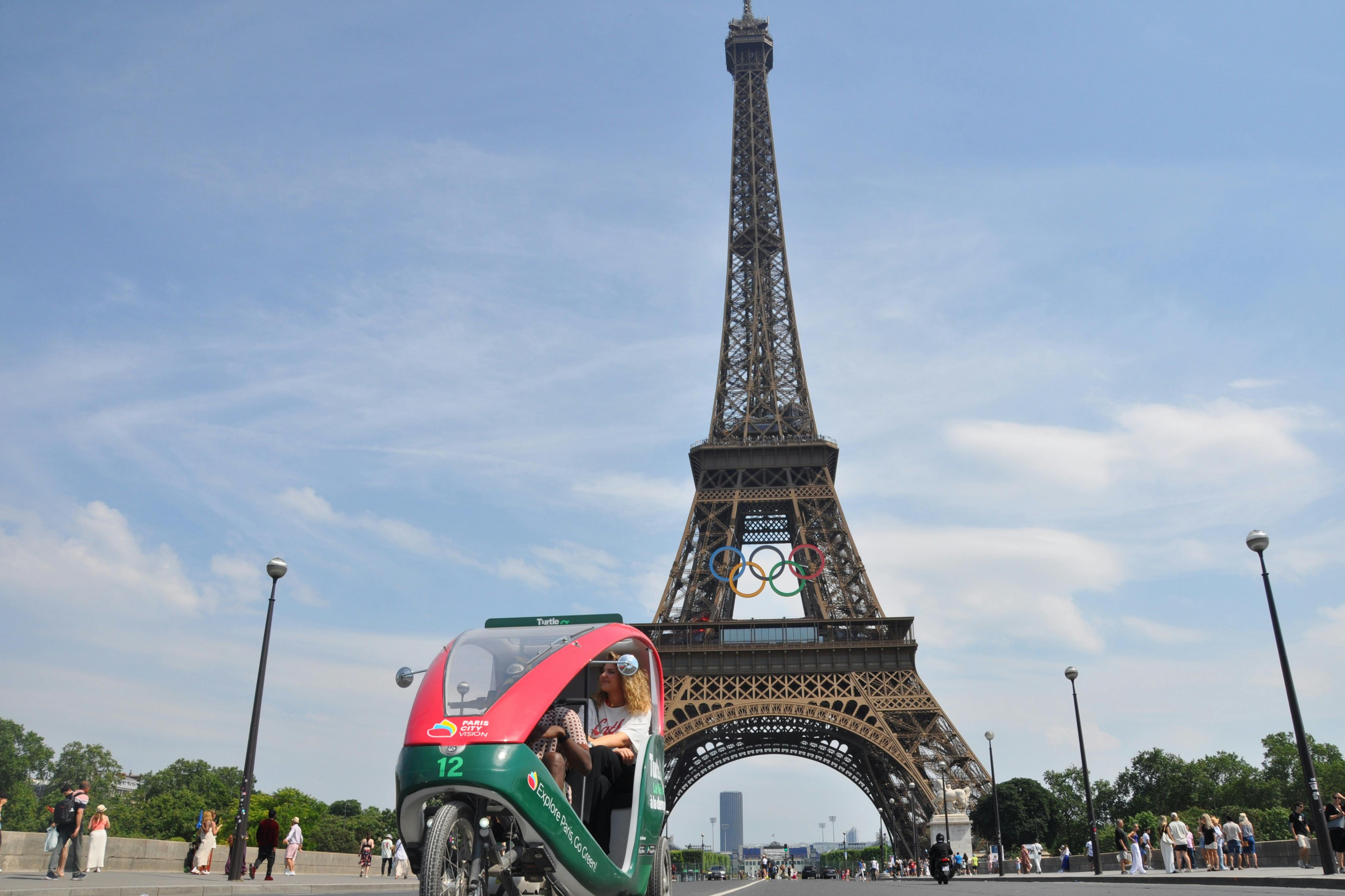 オリンピックリングが展示されたエッフェル塔の前に乗客を乗せた三輪車のペディキャブ。