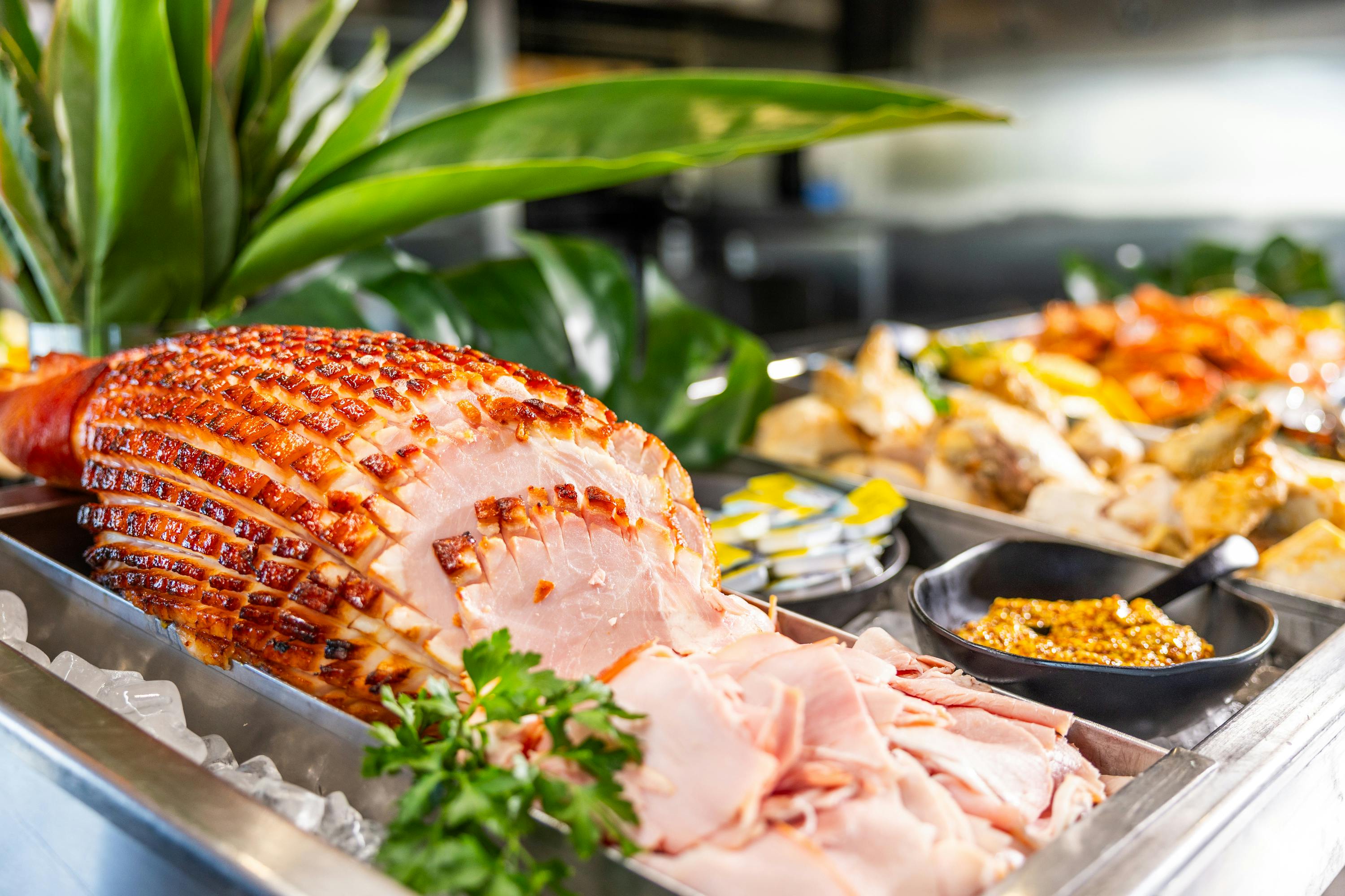 Σκαλιστό ζαμπόν γαρνιρισμένο με μαϊντανό, που εμφανίζεται σε μπουφέ με άλλα πιάτα στο παρασκήνιο.