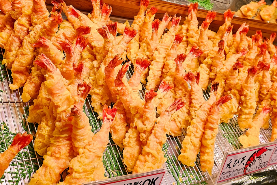 Multiple pieces of shrimp tempura arranged in rows on a metal rack, ready for serving.