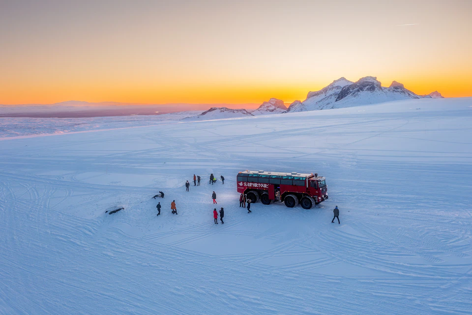 Drone shot of tourists outside on the glacier during beautiful sunset