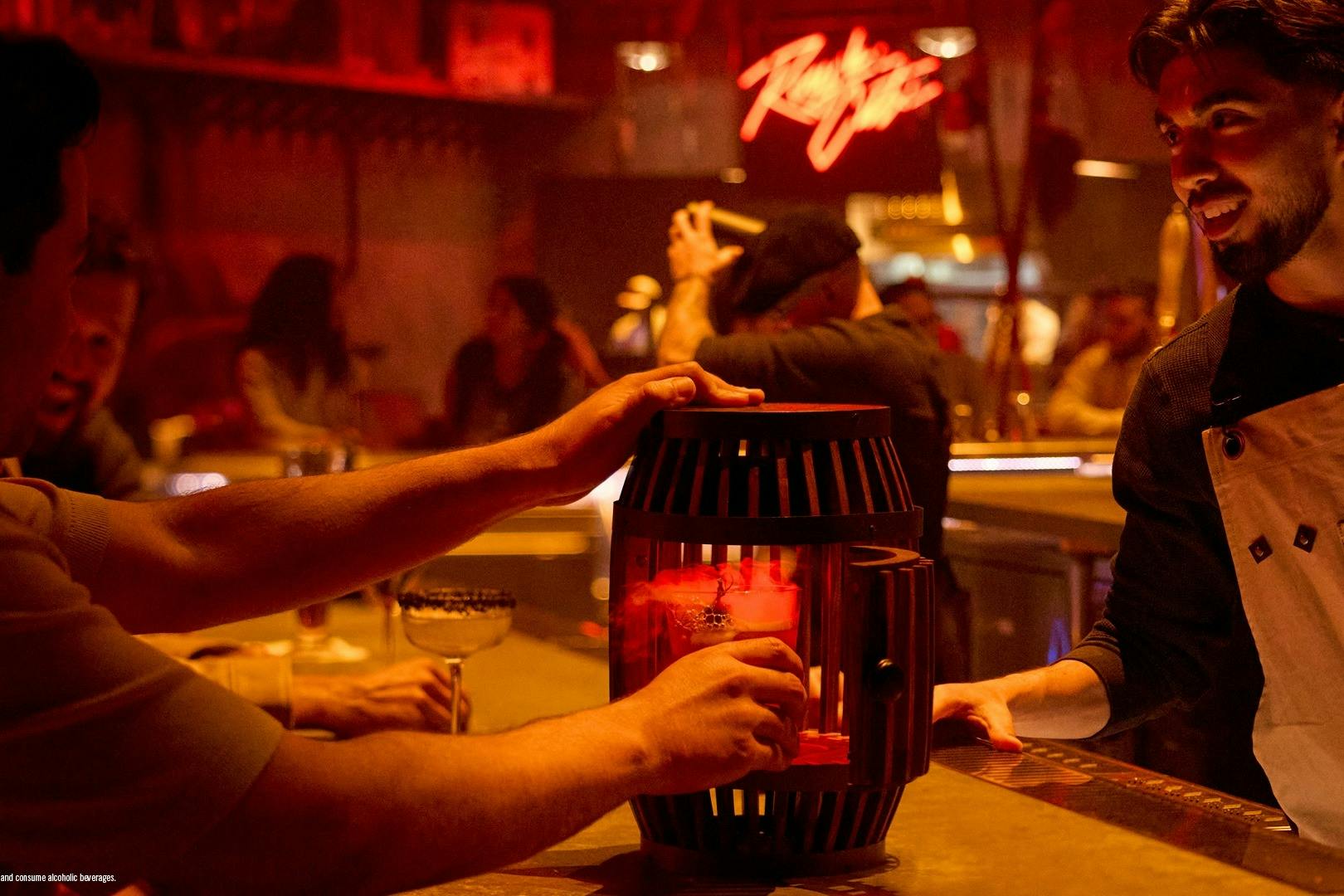 사람들은 네온사인을 배경으로 조명이 어두운 방 중앙에 빨간 등불이 켜진 바 테이블에 모여듭니다.