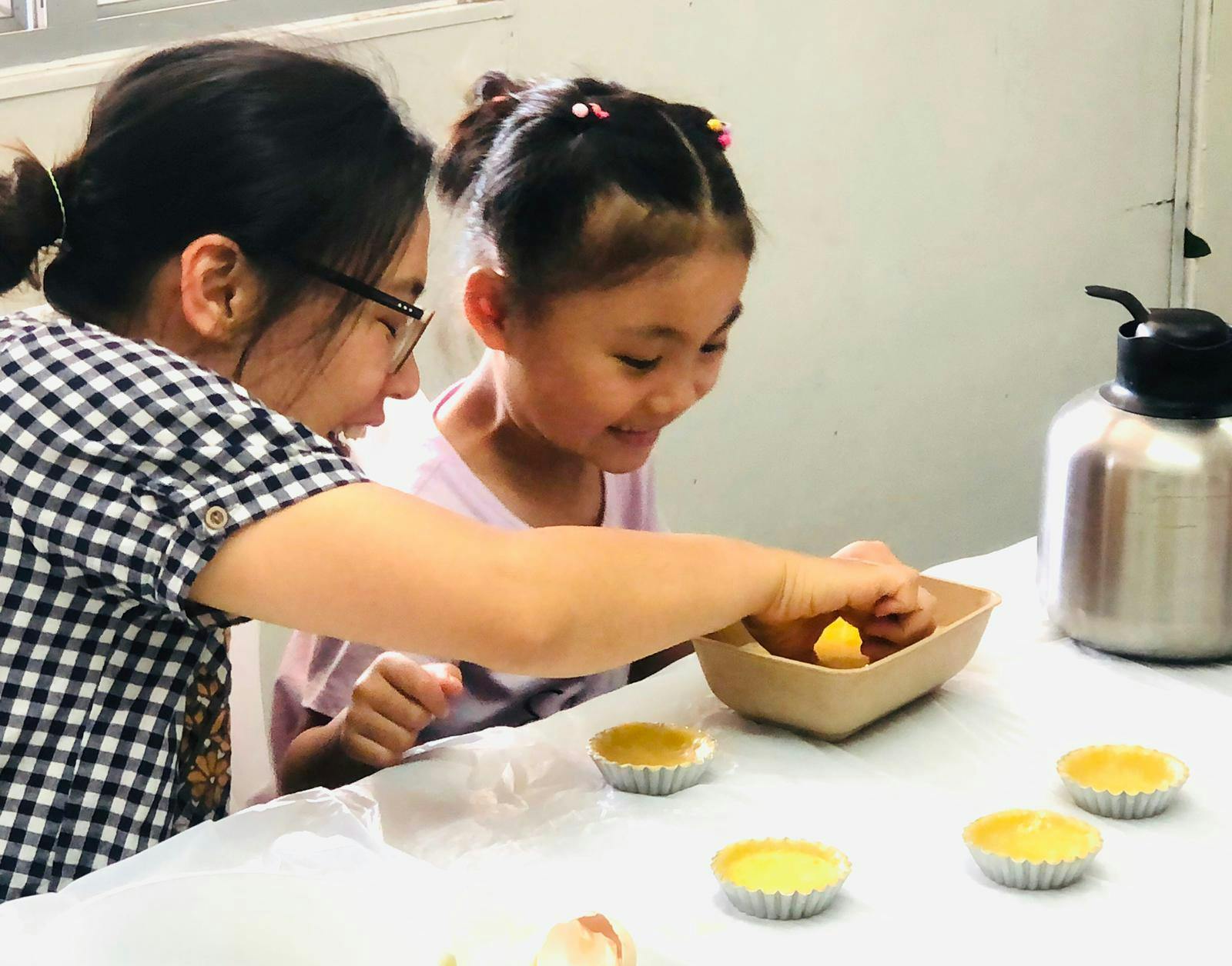 An adult and a child are sitting at a table, engaging in a baking activity with dough and small molds.
