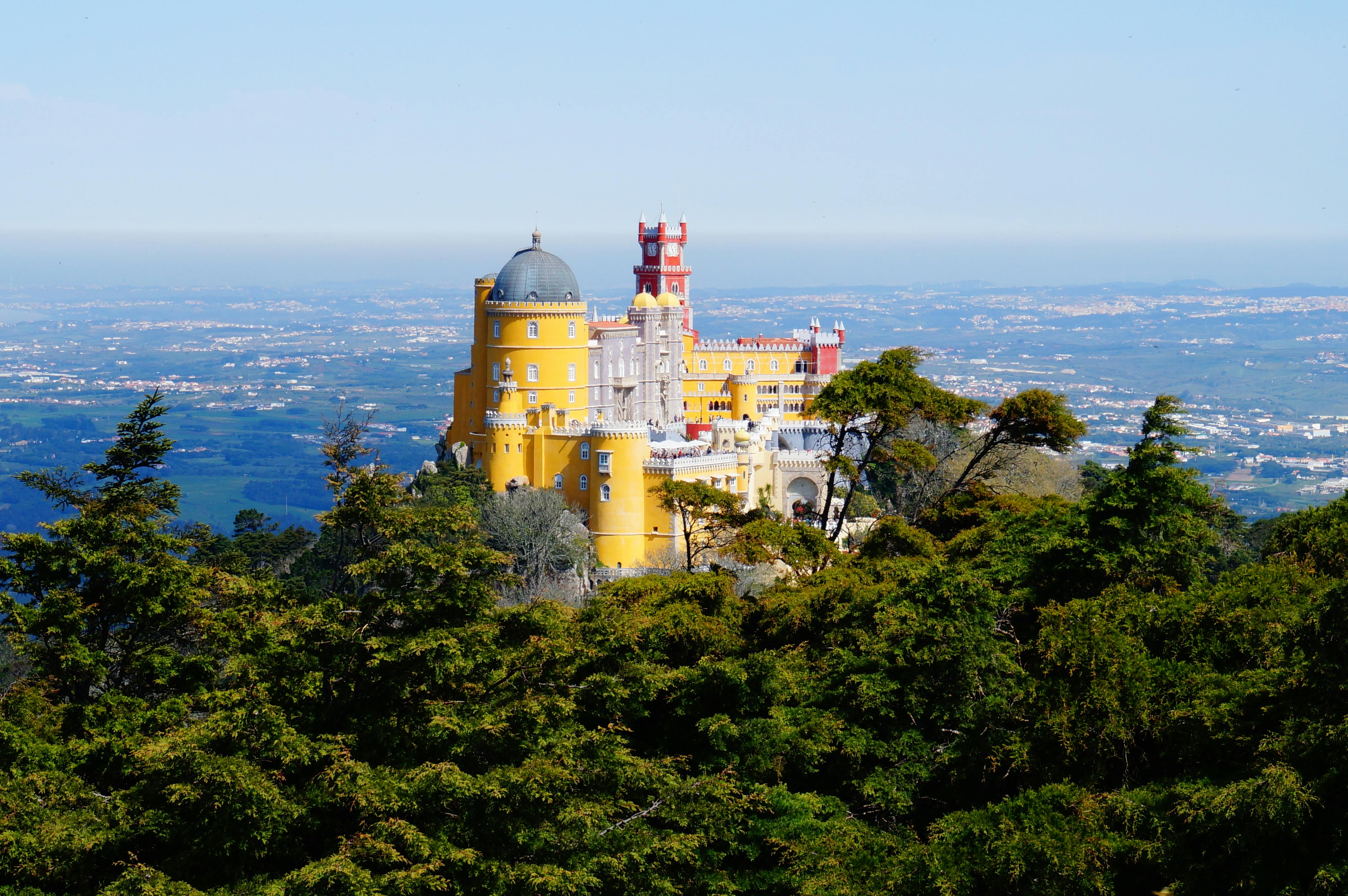 緑豊かな丘の上には、黄色、赤色、白色の塔を備えたカラフルで華やかな城があり、広大な風景を背景にしています。