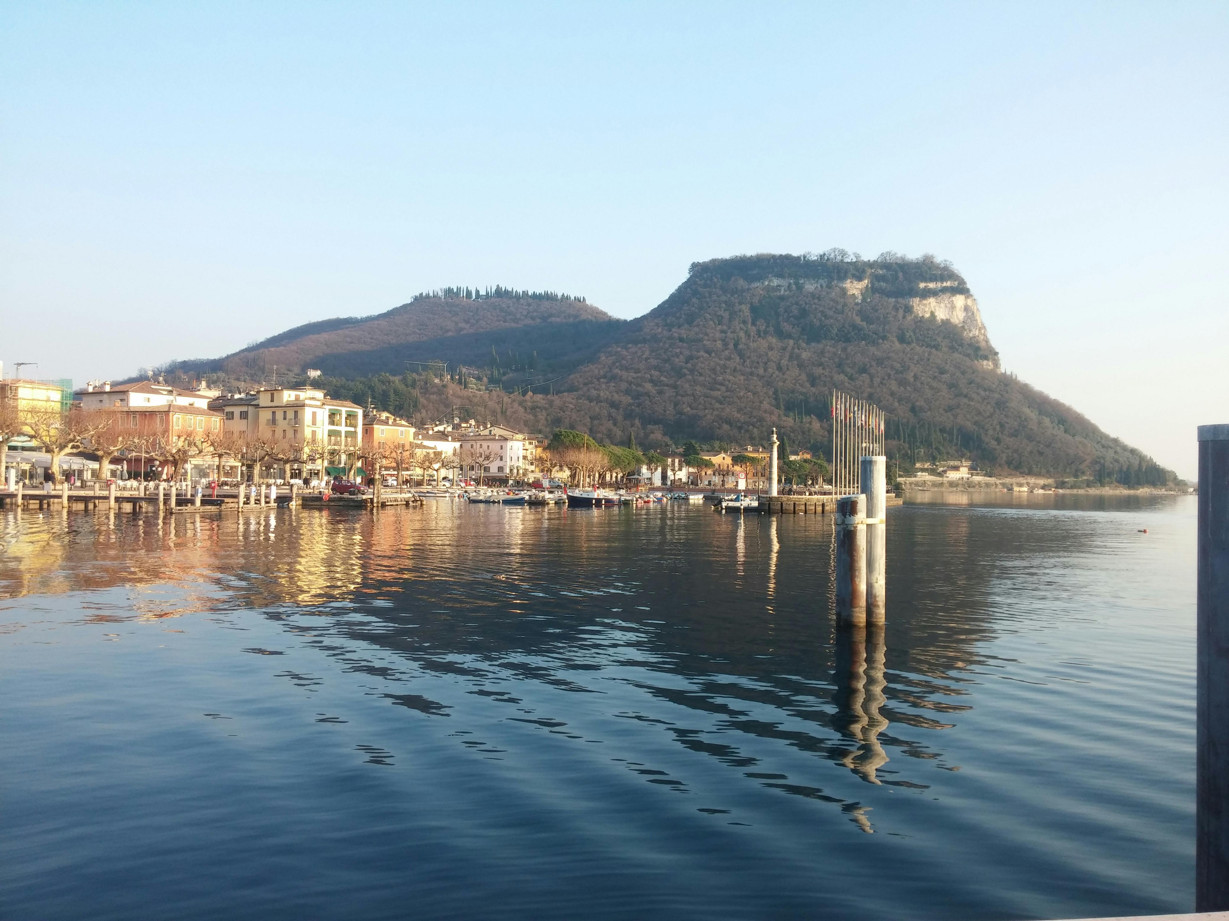 Una città sul lago con edifici colorati, una montagna sullo sfondo e l'acqua calma che riflette il paesaggio.