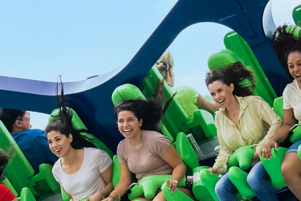 People seated on a green amusement ride suspended high in the air, with a blue sky and clouds in the background.