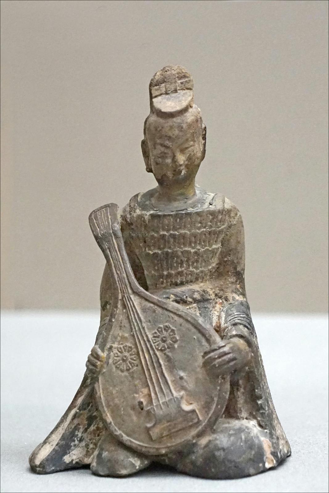 一尊磨损的古老雕塑，雕塑中的坐姿演奏着弦乐器，可能是琵琶，顶部有绳结。