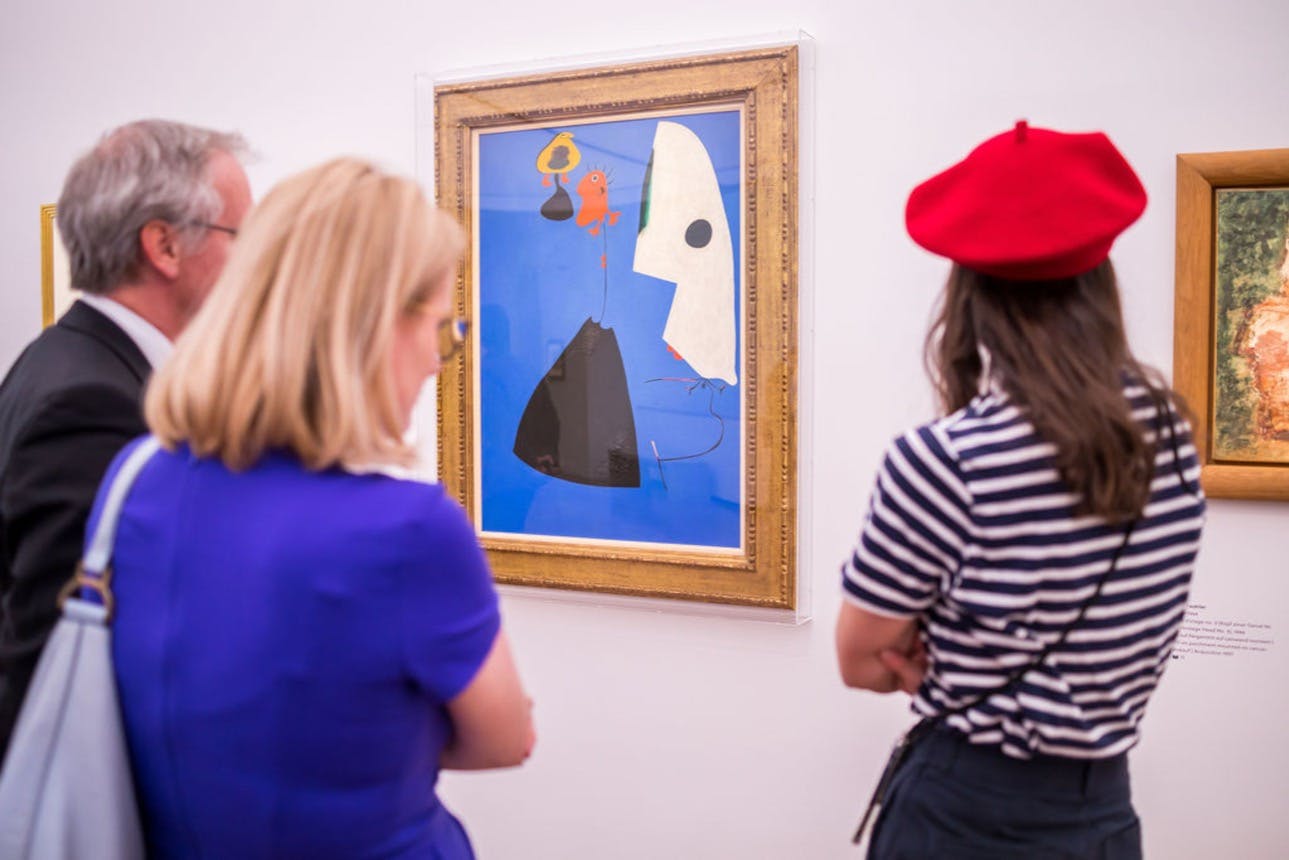 Dva lidé si prohlížejí zarámovaný abstraktní obraz s živými modrými a oranžovými odstíny v umělecké galerii.