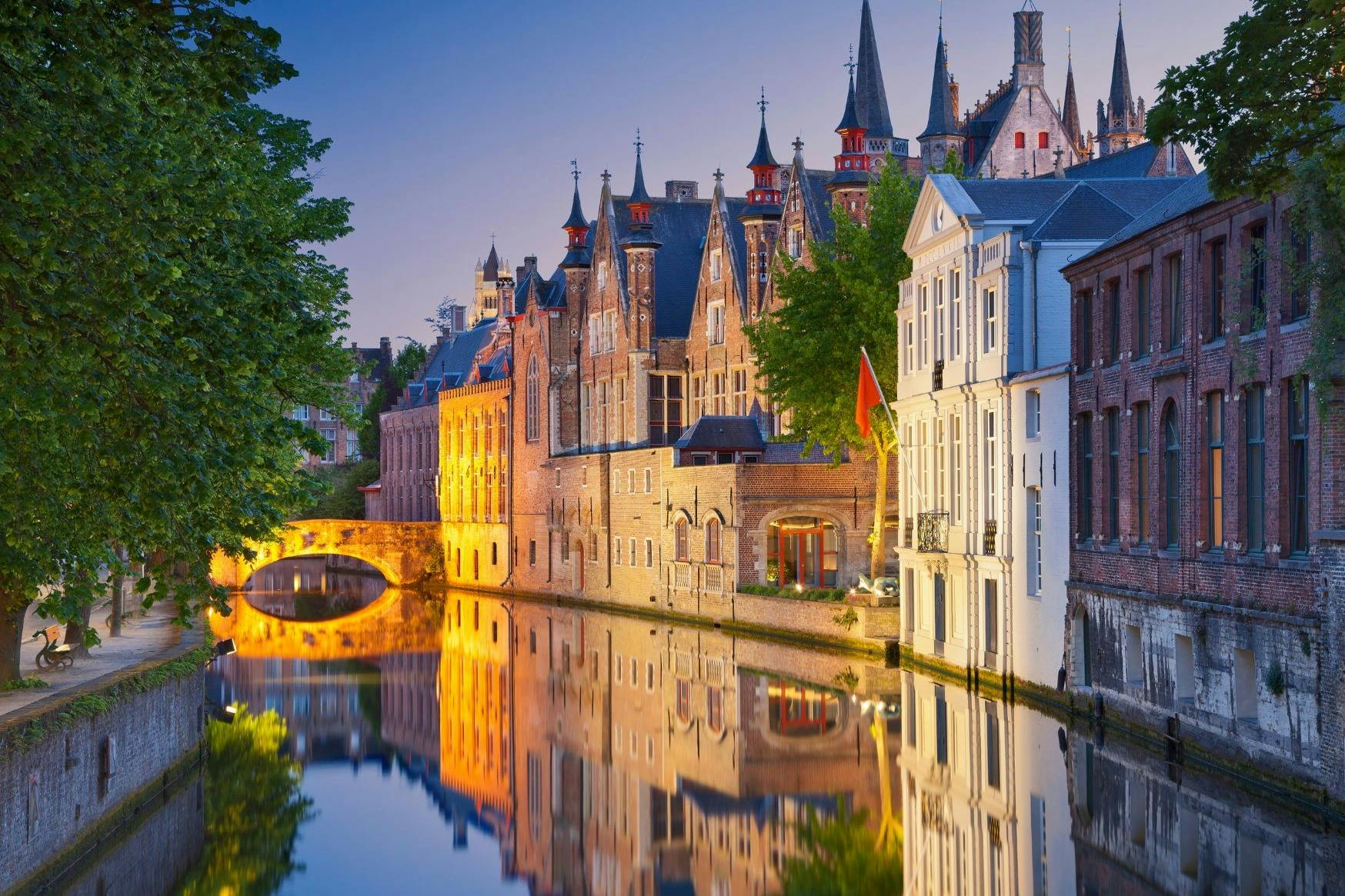 黄昏时分，历史悠久的建筑反映在一条平静的运河上，背景是华丽的建筑和一座石桥。