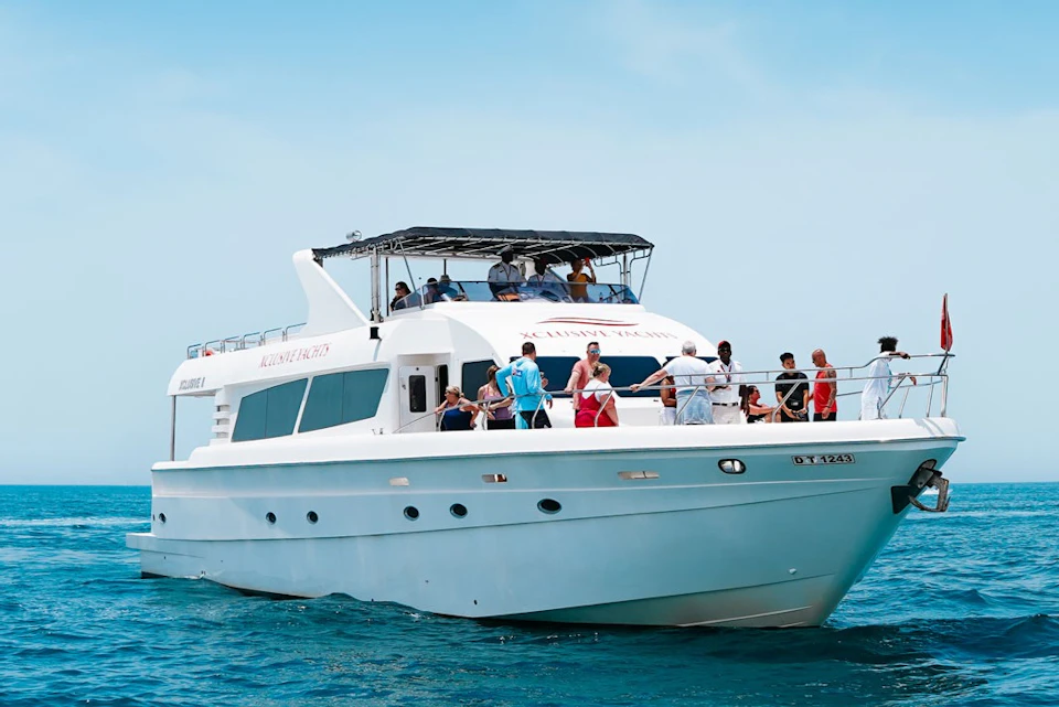 A white yacht on open water with several people on deck under a clear blue sky.