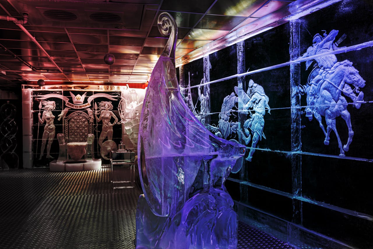 형형색색의 조명으로 빛나는 왕좌, 조각상, 바이킹 선박 등 정교한 얼음 조각이 있는 객실입니다.
