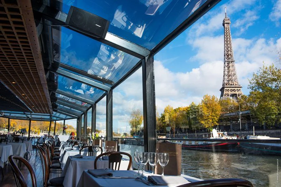 Barco restaurante de cristal en el Sena con vistas a la Torre Eiffel y árboles de otoño