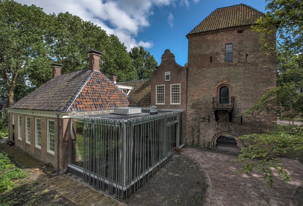 부분적으로 흐린 하늘 아래 나무로 둘러싸인 현대적인 유리 연장으로 지어진 유서 깊은 벽돌 건물입니다.