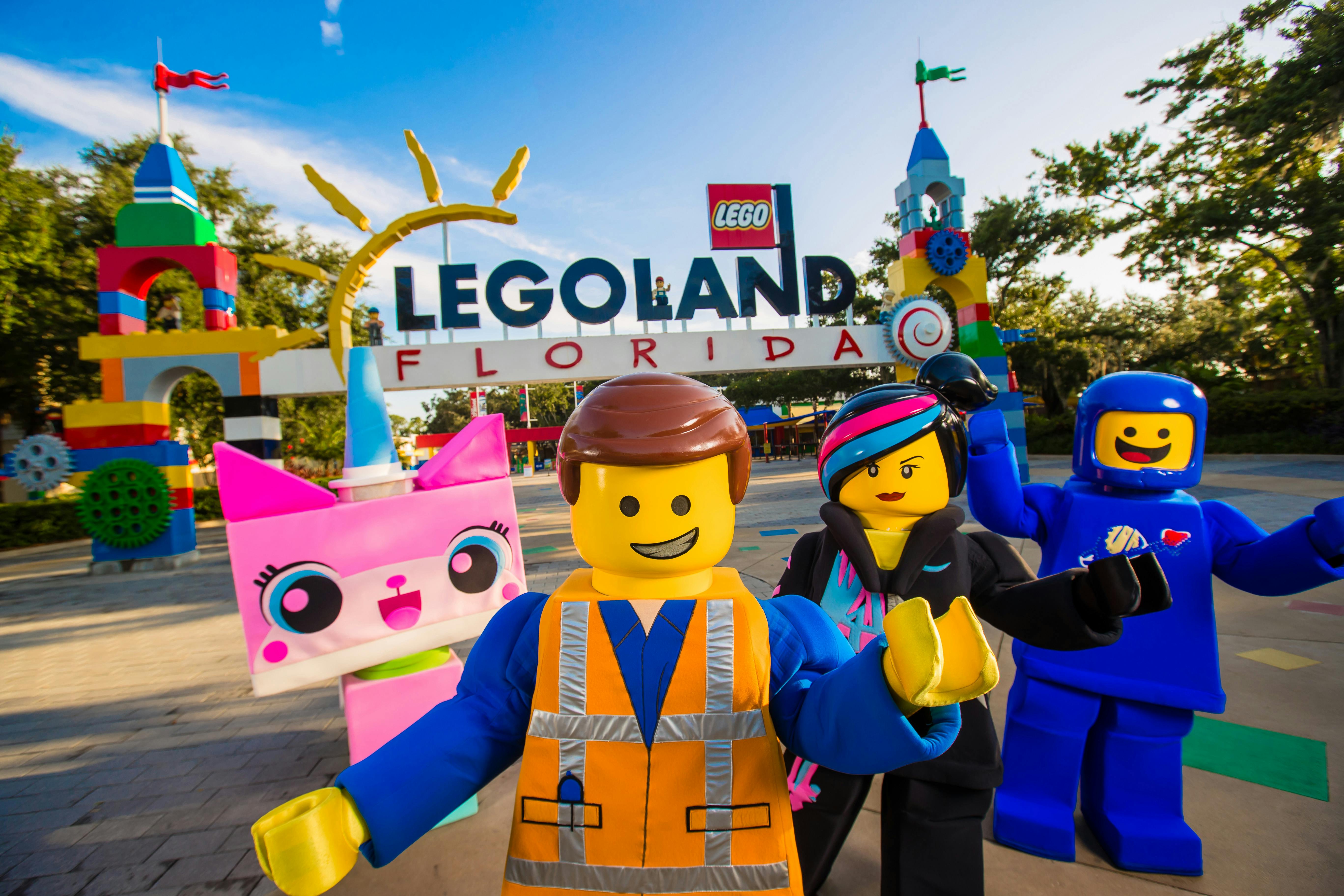Group of Lego character mascots standing in front of the Legoland Florida entrance sign.