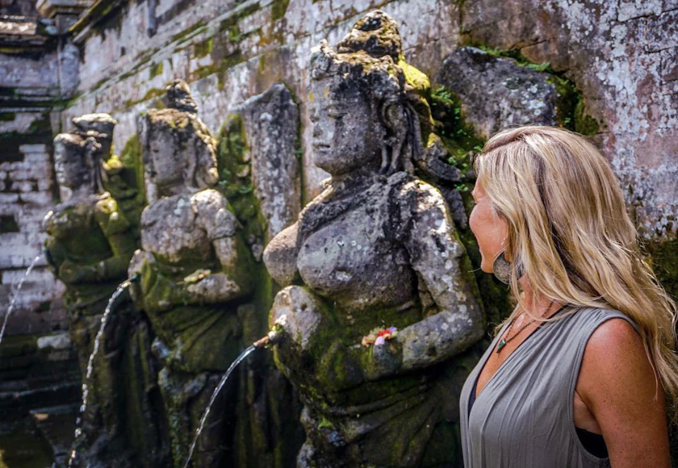 Three weathered stone statues with water spouts, set against an ancient, moss-covered brick wall.