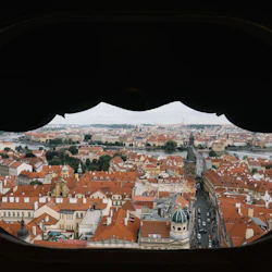 Utsikt över en stadsbild med byggnader med röda tak, en flod i bakgrunden och gator kantade med bilar, sedda genom en valvgång.