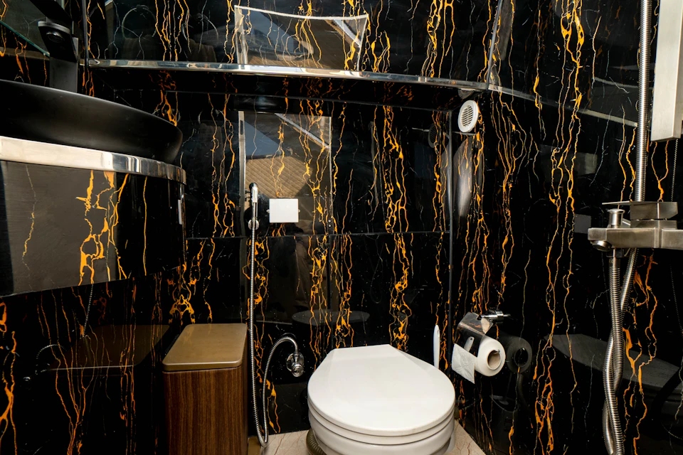 A small bathroom with black and orange marbled walls, a modern toilet, and a stainless steel shelf above.