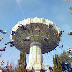 En svängkaruselltur snurrar med personer som sitter på svängande stolar mot en blå himmel, omgiven av träd.