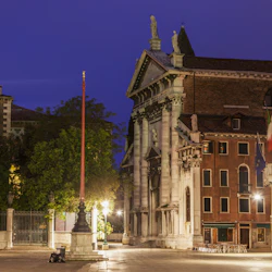 Tomt torg i skymningen med historiska byggnader, inklusive en kyrka och en gata med uteservering. Dämpade gatubelysning lyser upp scenen.