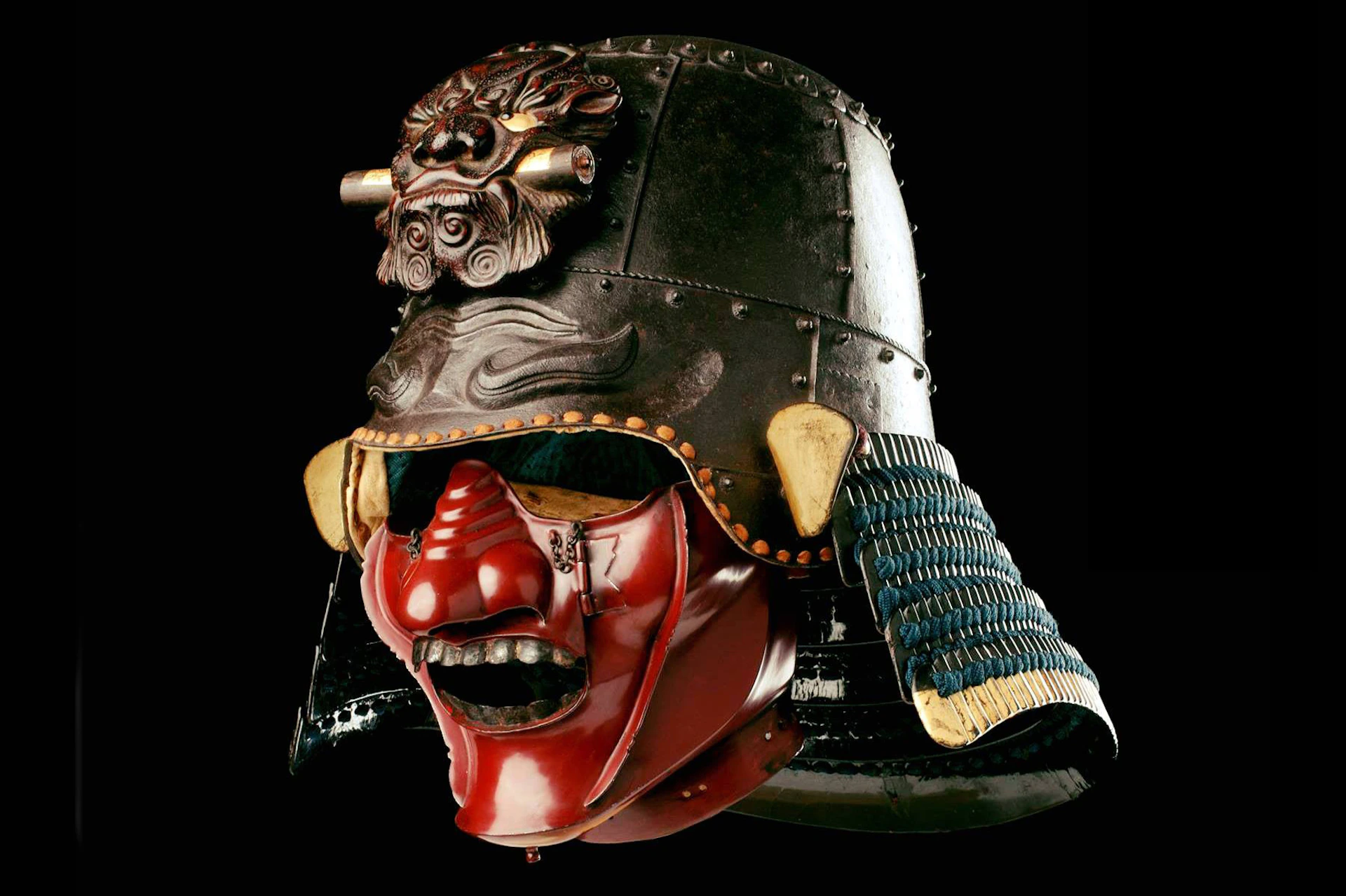 A traditional Japanese samurai helmet with a red face mask and intricate decorations, displayed against a black background.