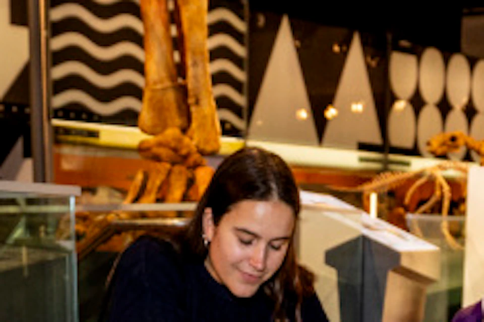 A guide with a headset gestures toward a fossil exhibit on the floor, while two people crouch and observe it intently.
