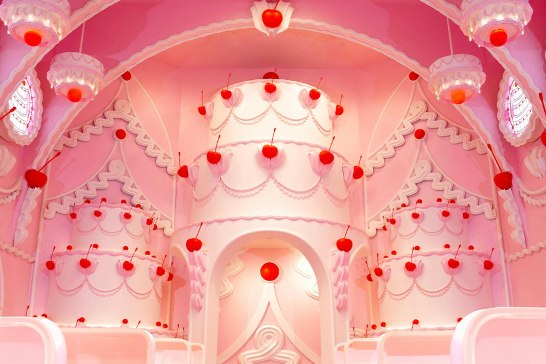 A whimsical pink interior with cake-like structures adorned with red cherries and decorative designs.