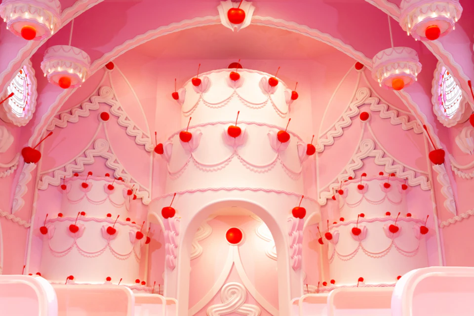 A whimsical pink interior with cake-like structures adorned with red cherries and decorative designs.