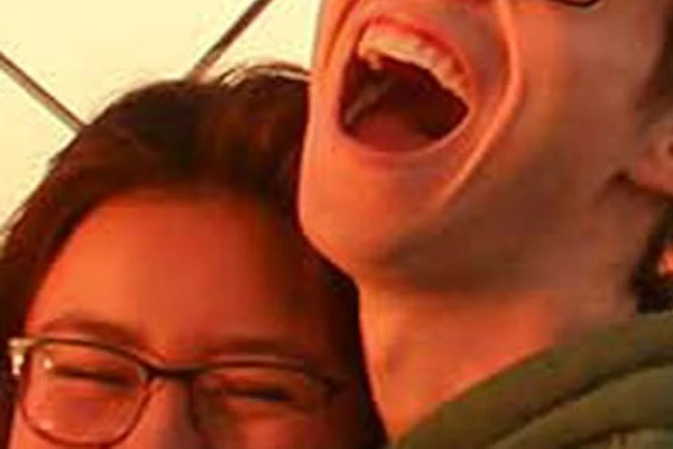 Two people smiling and hugging on an observation deck with a cityscape and a viewing scope in the background.