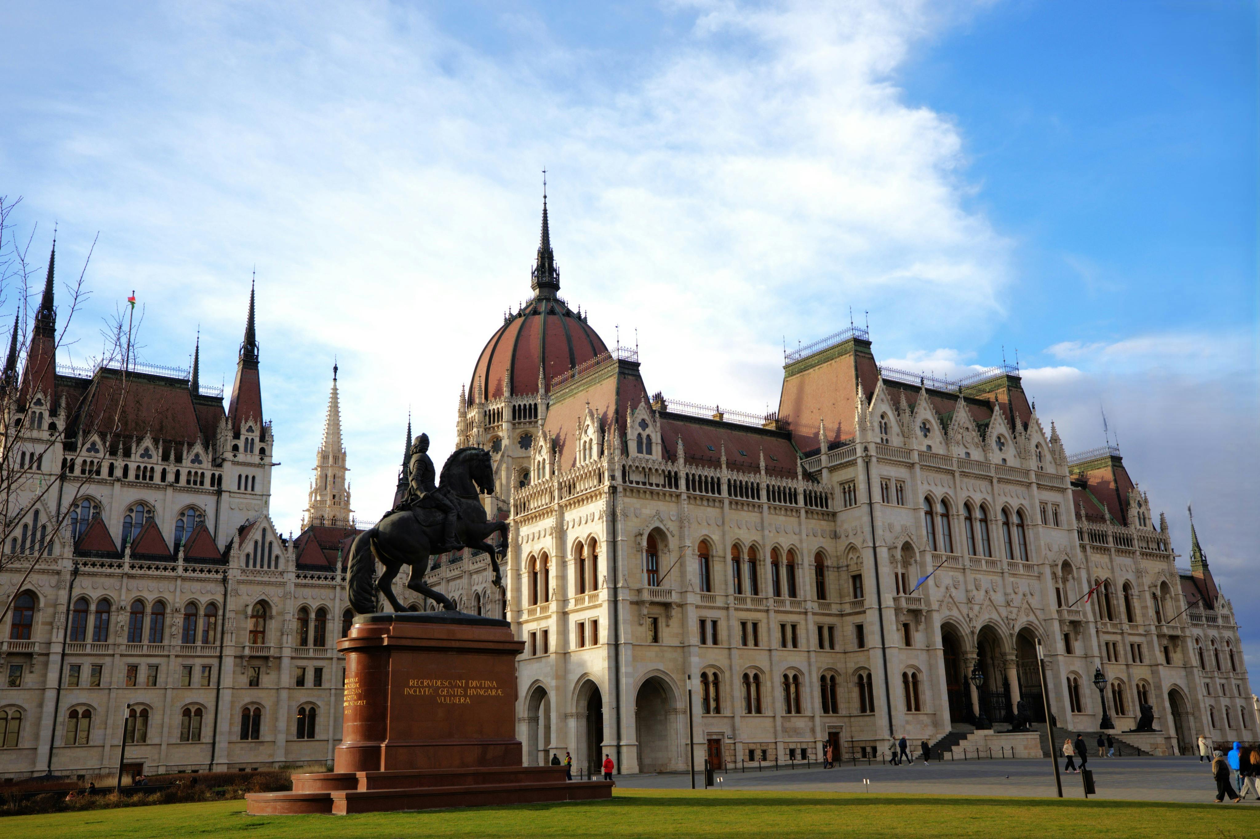 A statue of a rider on horseback in front of a large ornate building with multiple spires and a dome under a blue sky.