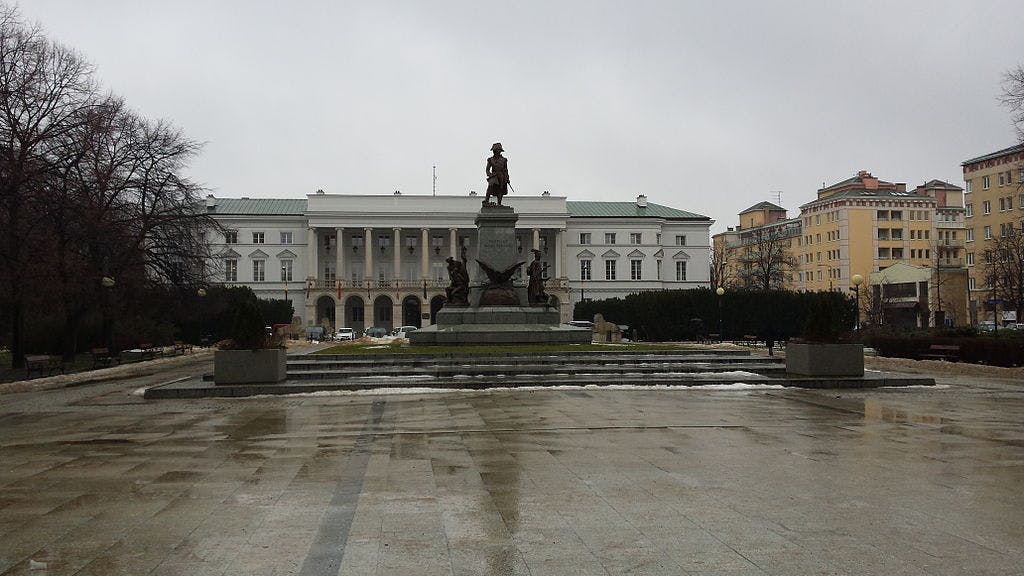 Estàtua de Copèrnic davant del palau Staszic, amb el paviment humit, els arbres sense fulles i els edificis circumdants sota un cel ennuvolat.