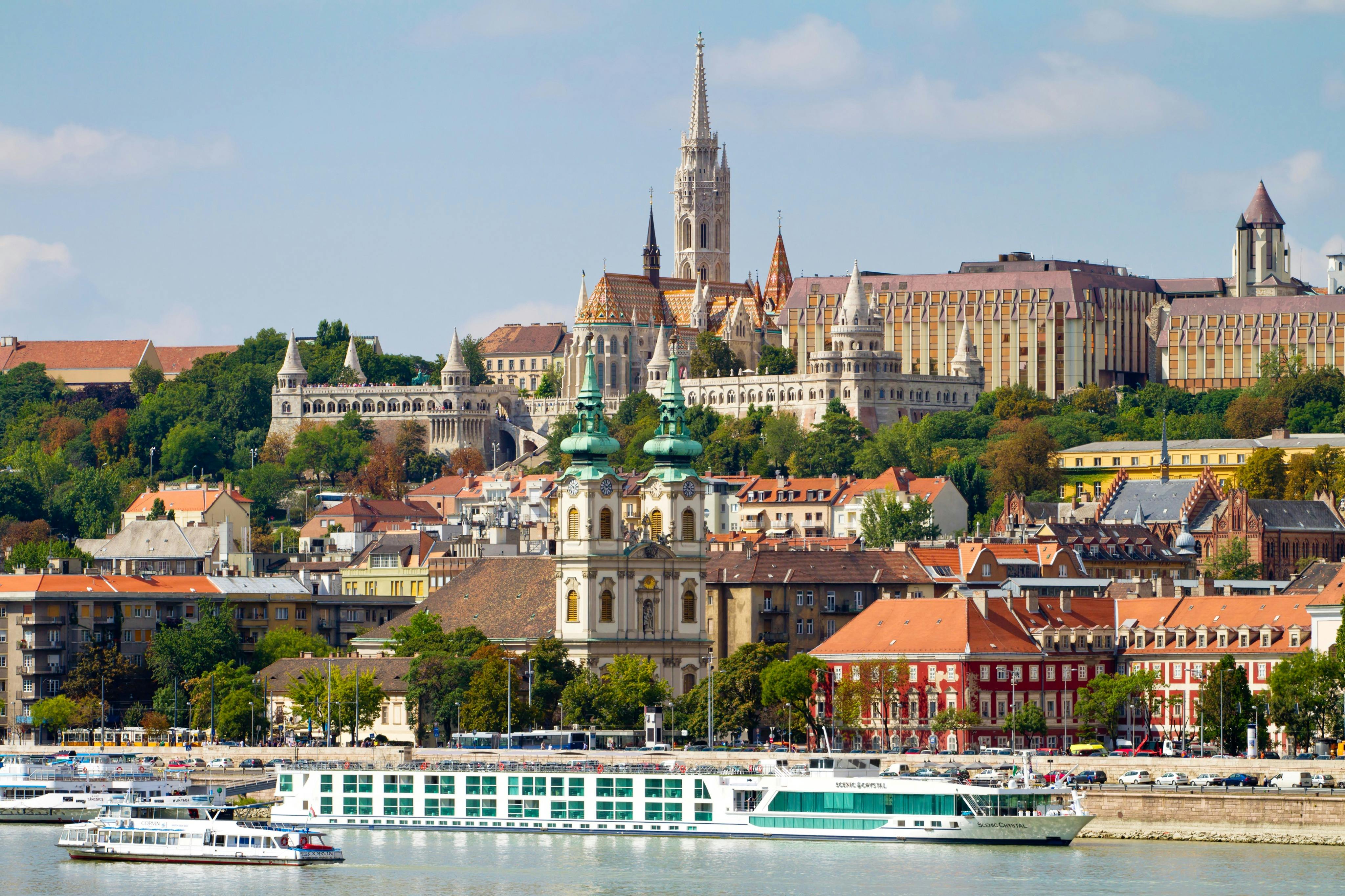 A riverside cityscape featuring historical architecture, a church with spires, and a large riverboat in the foreground.