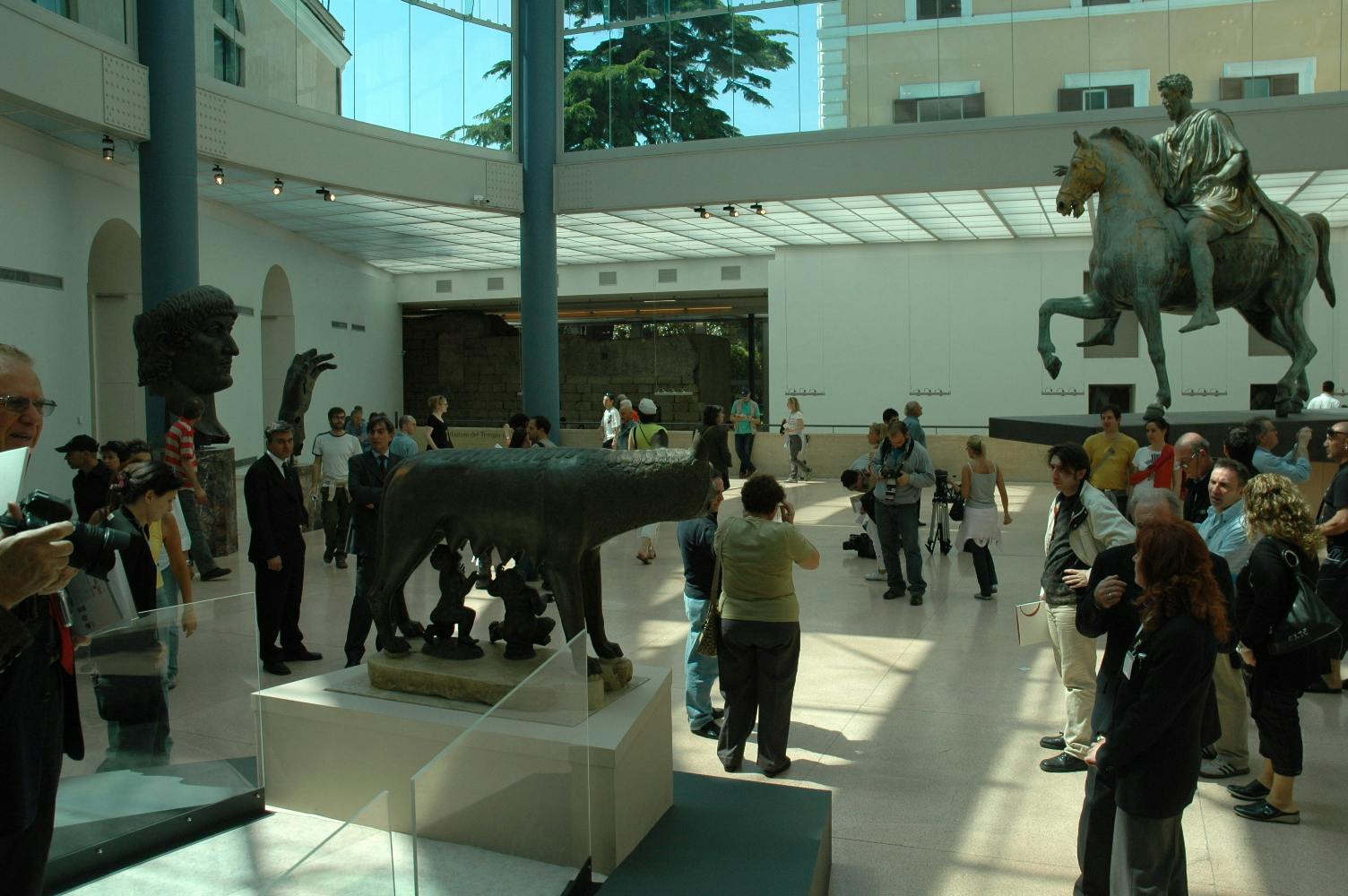 People touring a museum with a statue of a man riding a horse and another of a wolf nursing two infants.