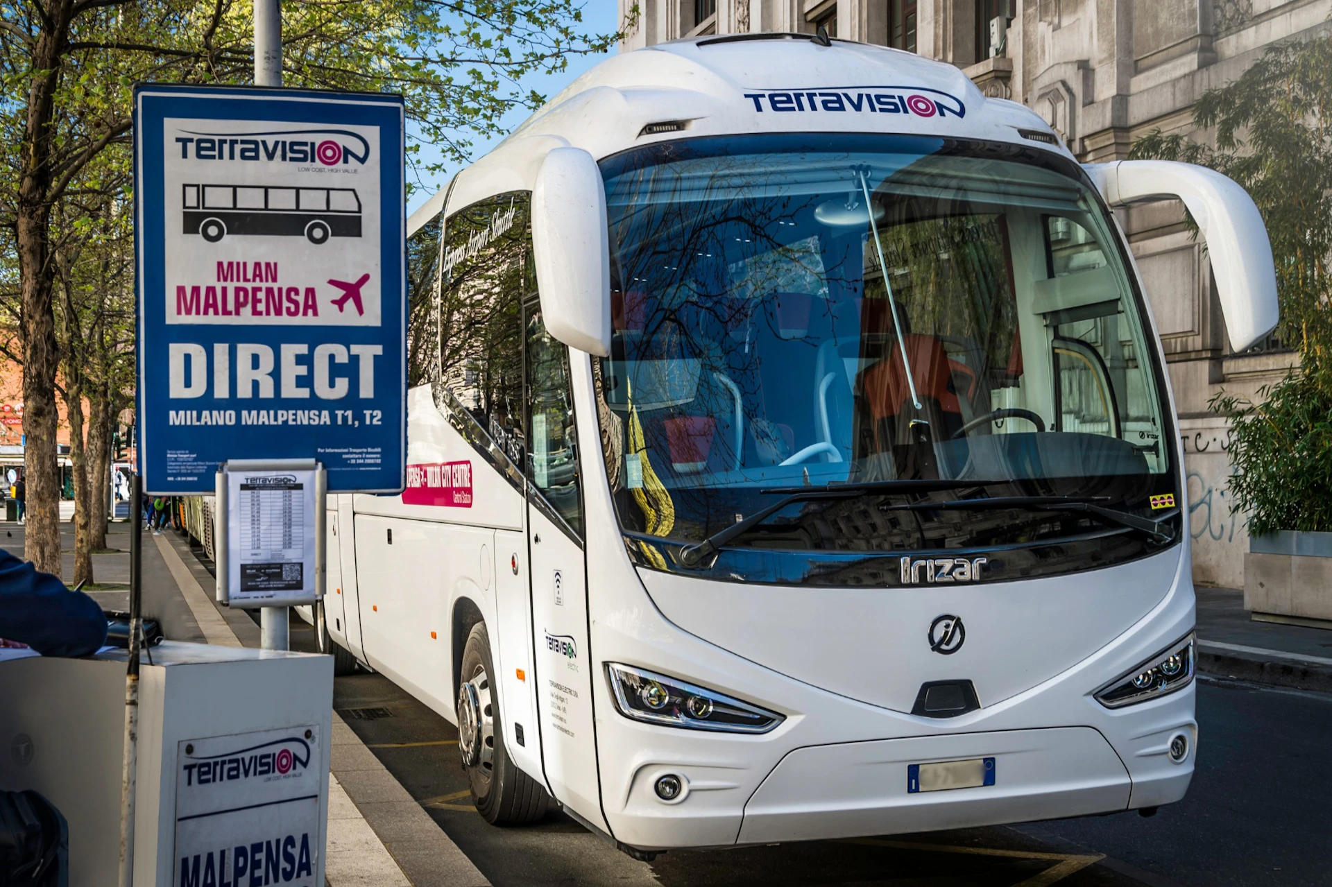 A white Terravision bus is parked next to a sign for direct service to Milan Malpensa Airport.