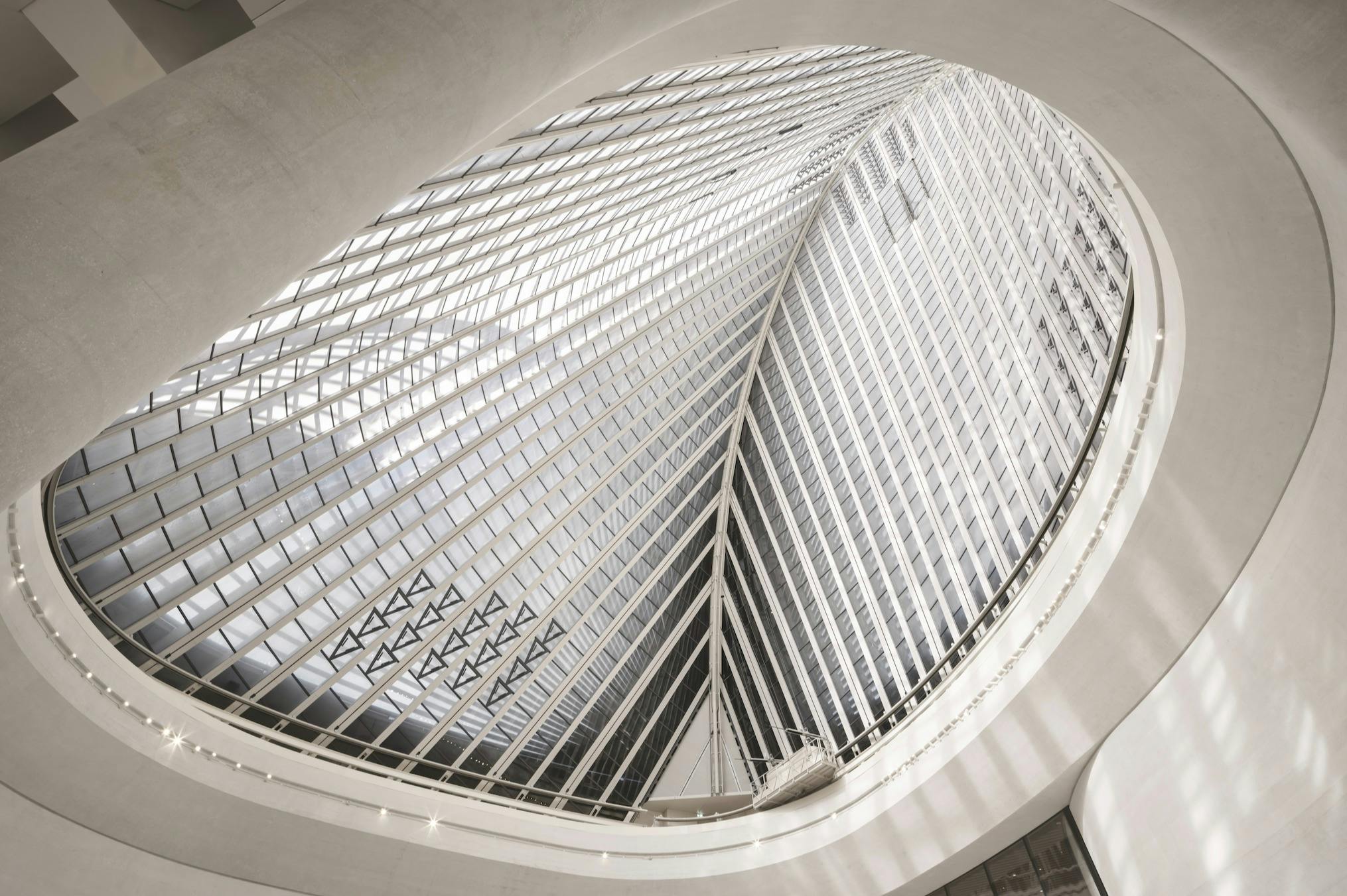 Vnitřní pohled na moderní budovu s velkou zakřivenou skleněnou a ocelovou konstrukcí vytváří složitý vzor nad hlavou.
