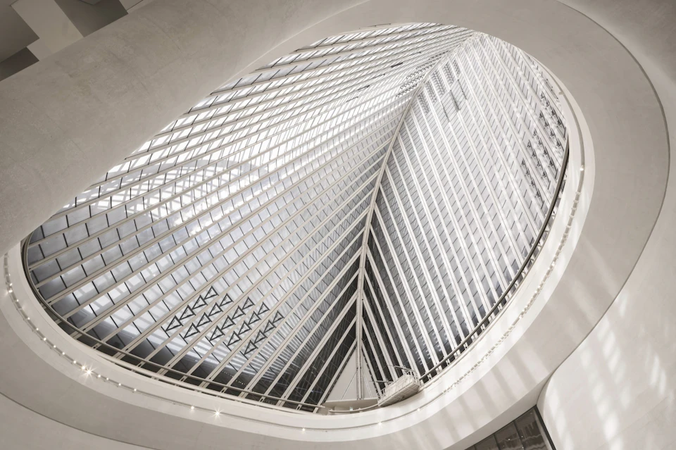 Interior view of a modern building with a large curved glass and steel structure creating an intricate pattern overhead.