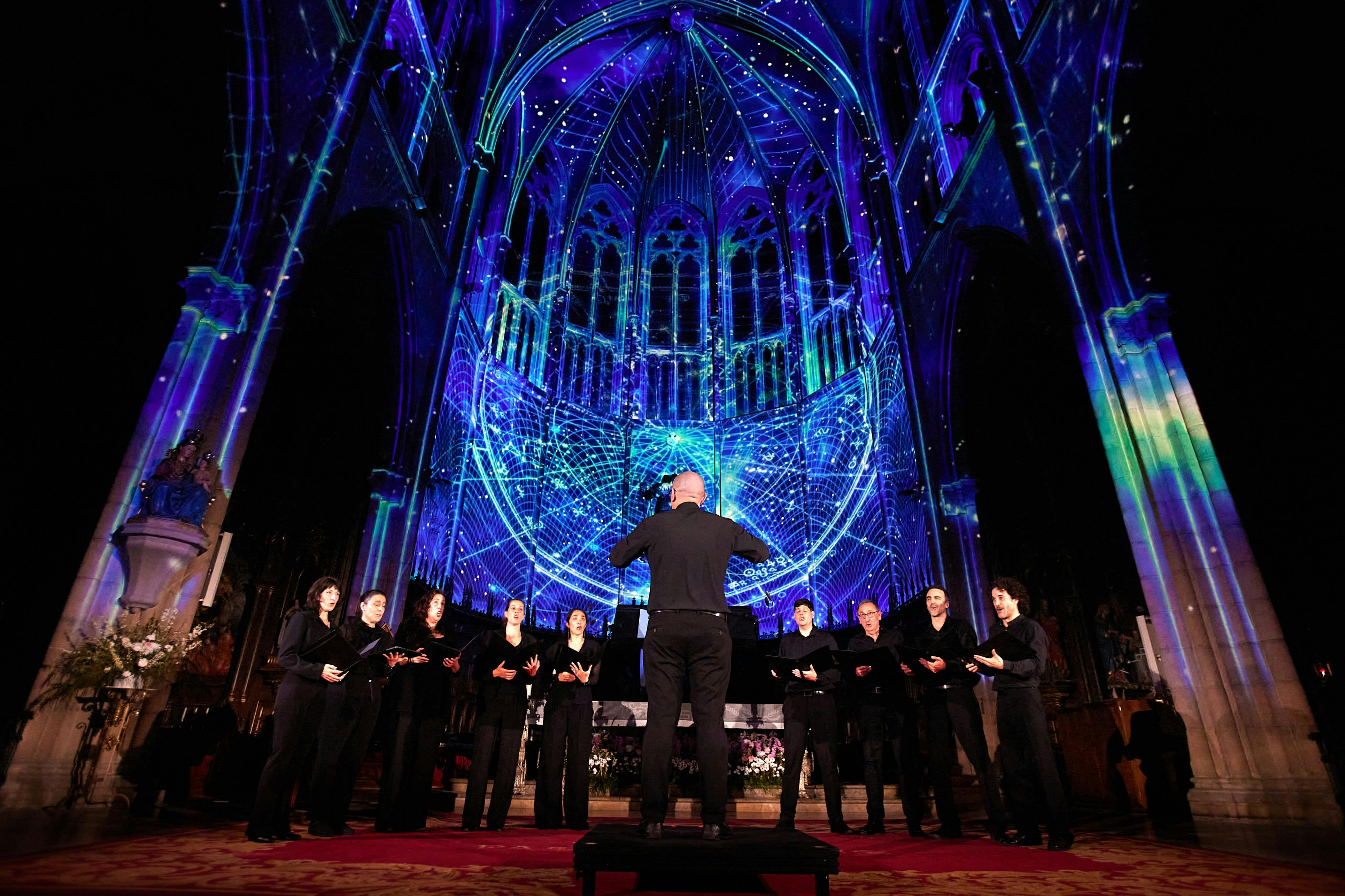 Une chorale se produit sous les arches d'une cathédrale illuminée par des motifs lumineux géométriques bleus et violets.