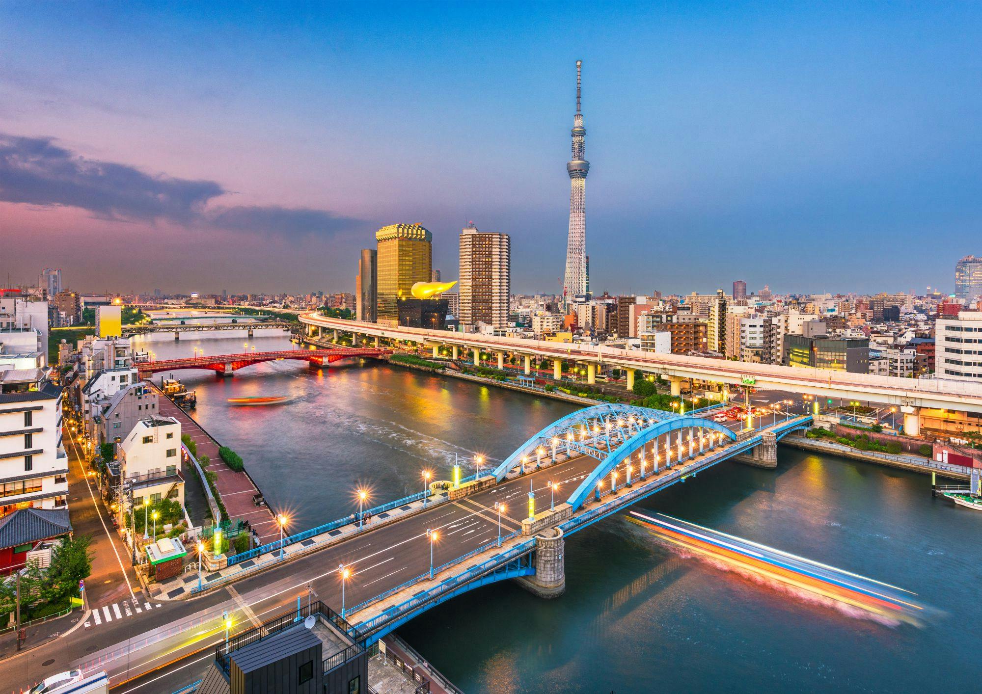 Cityscape with bridges over a river, the Tokyo Skytree in the background, and colorful lights reflecting on the water.