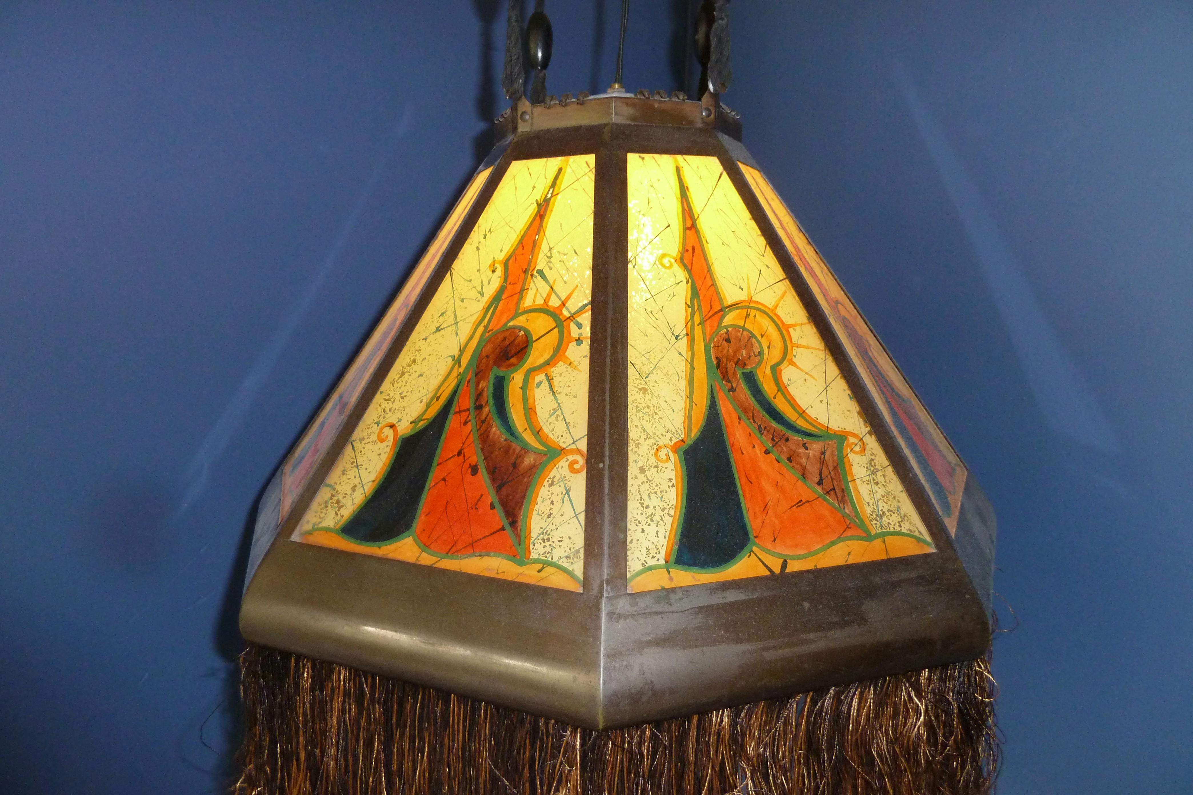 Na suficie pod niebieską ścianą wisi witrażowa lampa w geometryczne wzory w kolorze pomarańczowym, żółtym i zielonym.